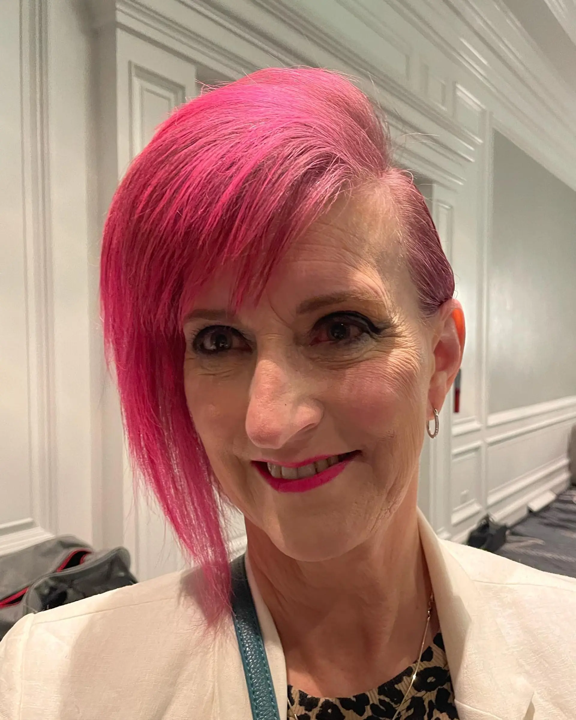 A bold asymmetrical pixie cut in an intense hot pink shade, featuring a close-cropped side and an elongated sweeping side fringe. 1