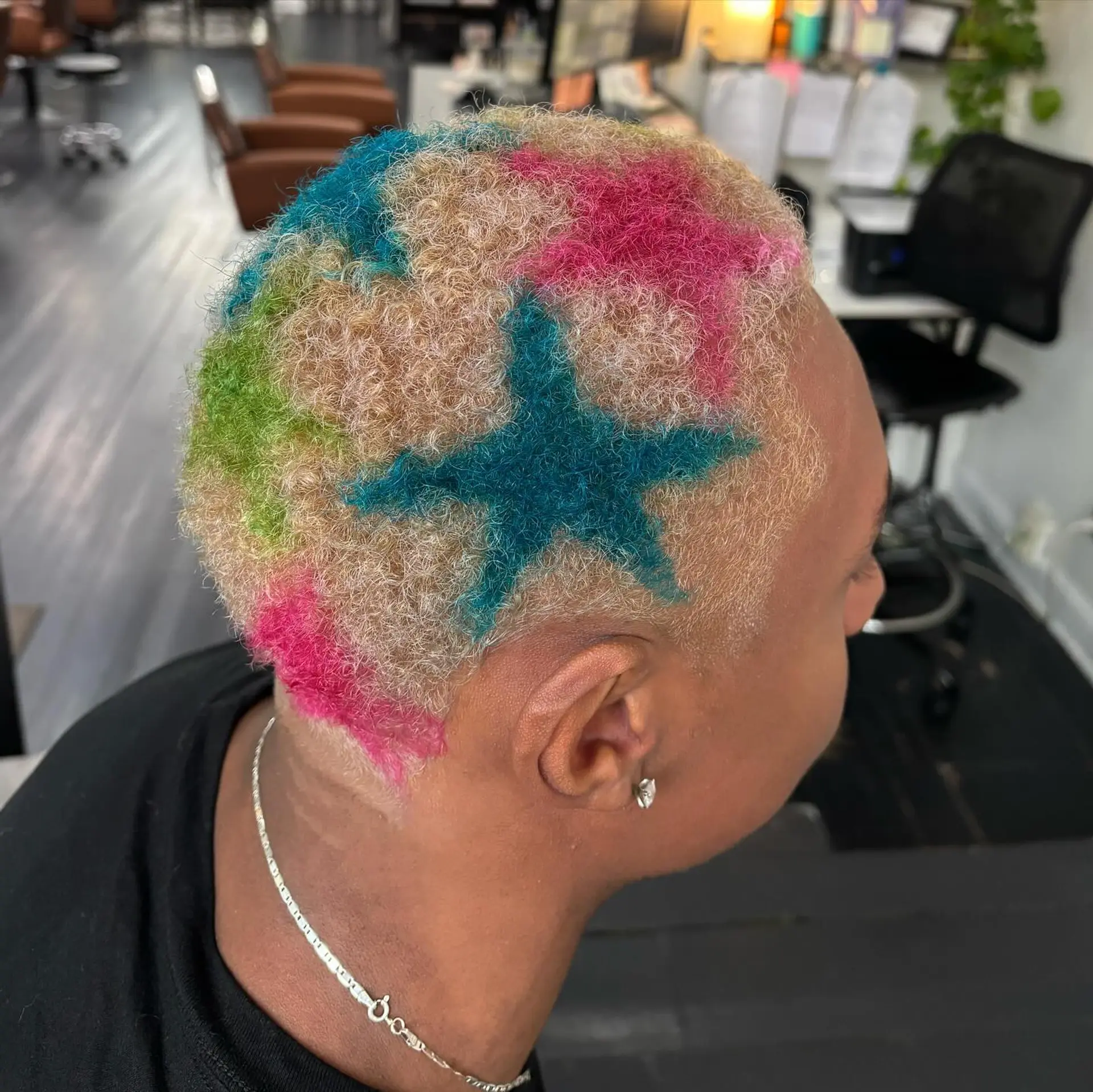Bleached blonde buzz cut decorated with vibrant, multicolored painted stars in shades of teal, hot pink, and green. 1