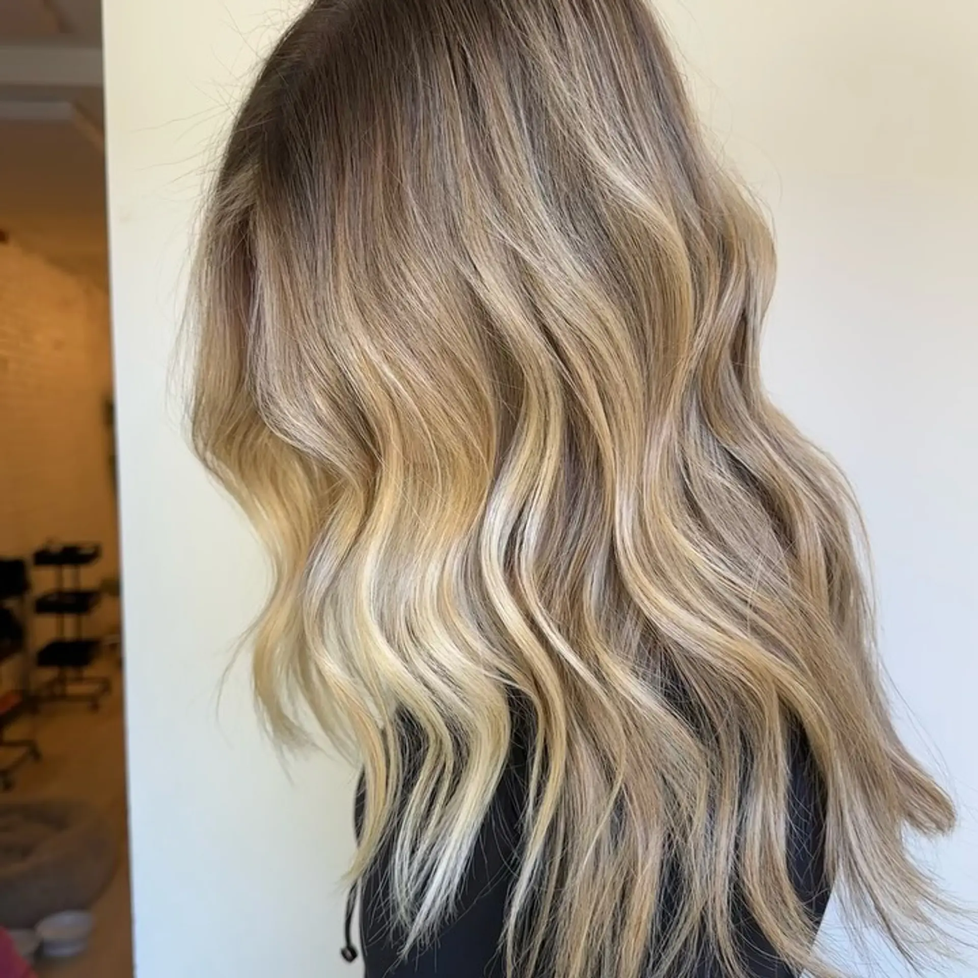 Long wavy hair with a seamless lived-in blonde balayage blending from natural darker roots to bright blonde ribbons. 1