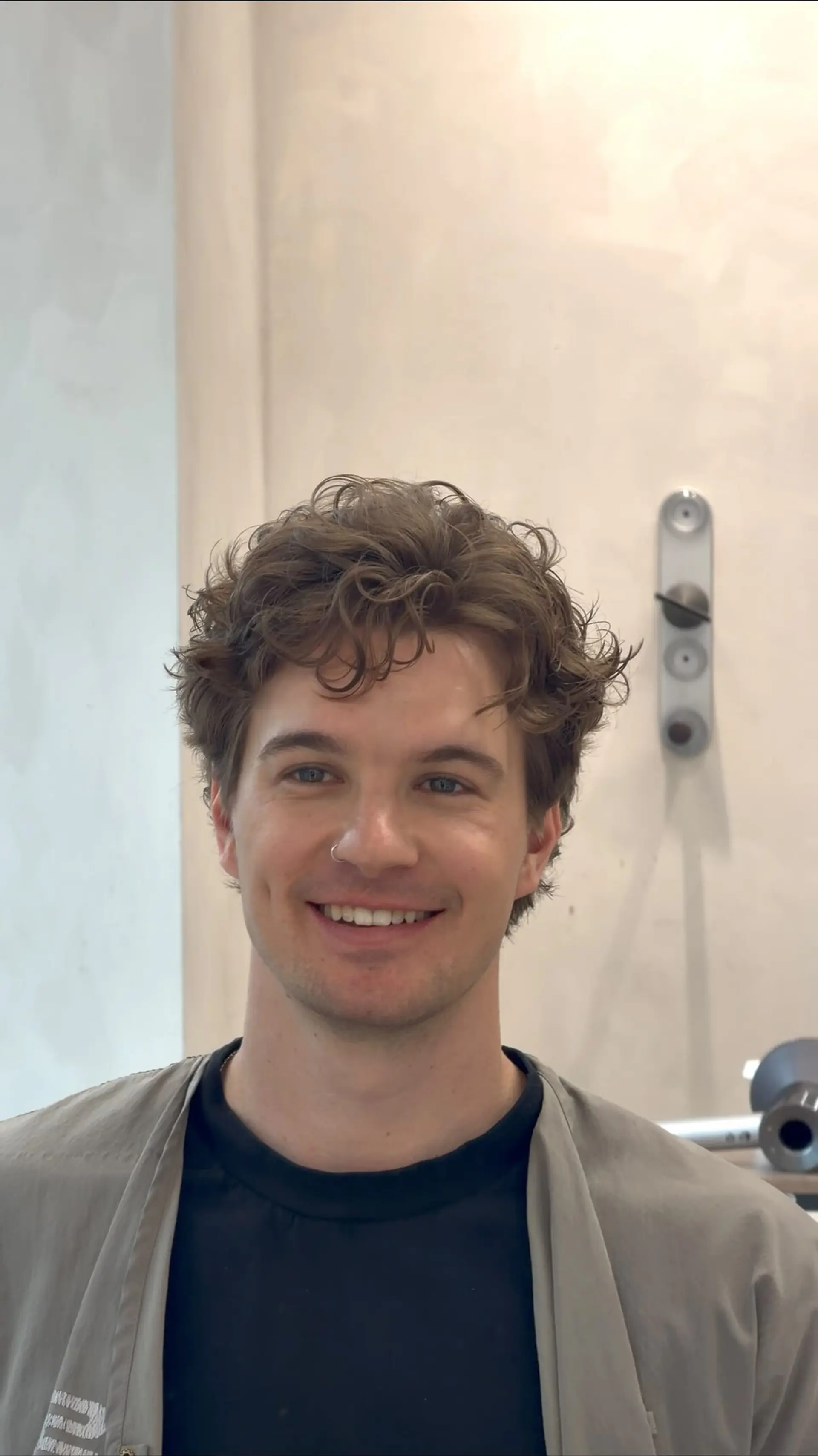A short, tousled men's haircut featuring loose wavy permed texture and soft fringe framing the forehead. 1