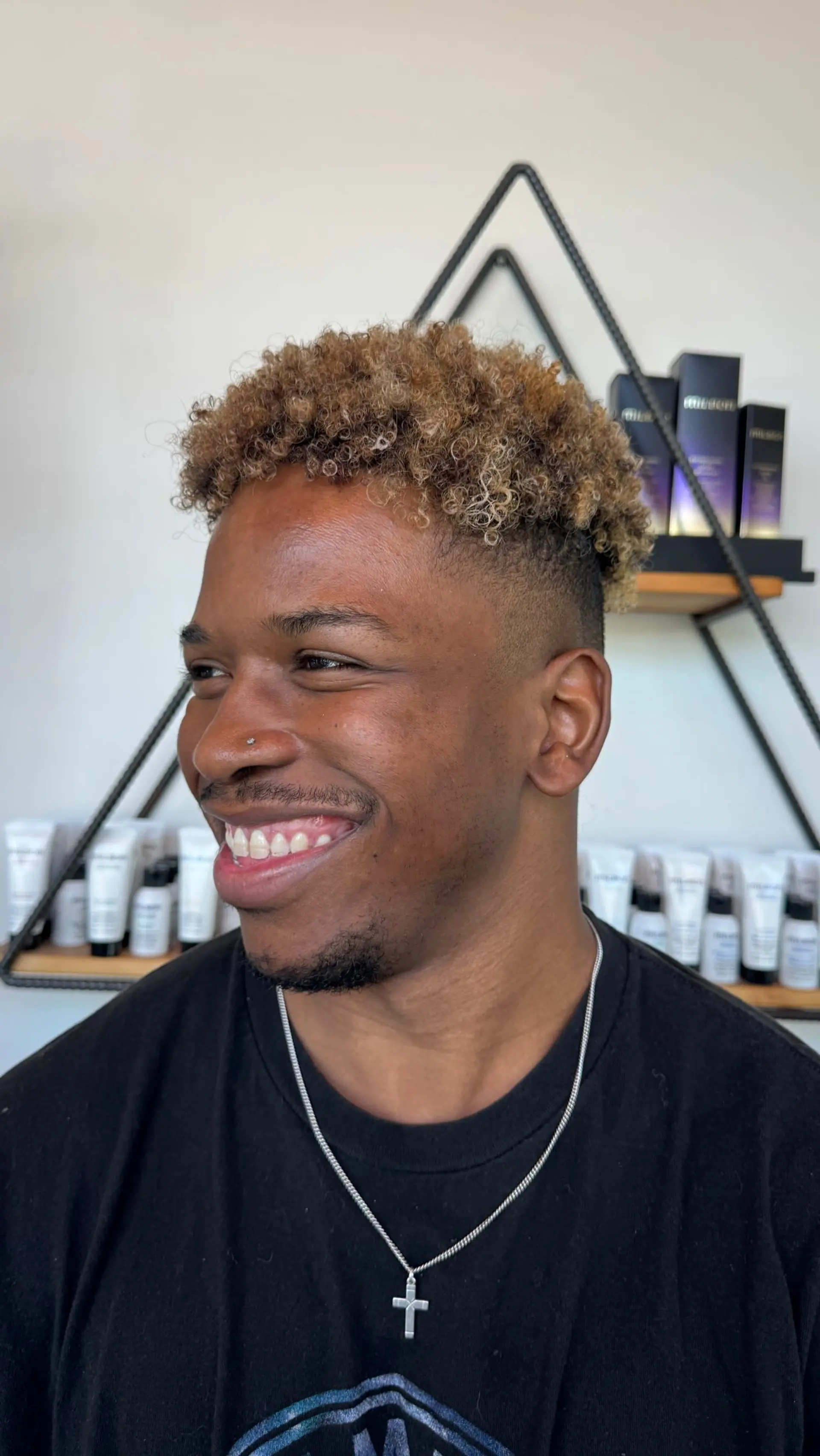 A short high-top haircut featuring tight honey blonde coils on top with a clean skin fade on the sides. 1