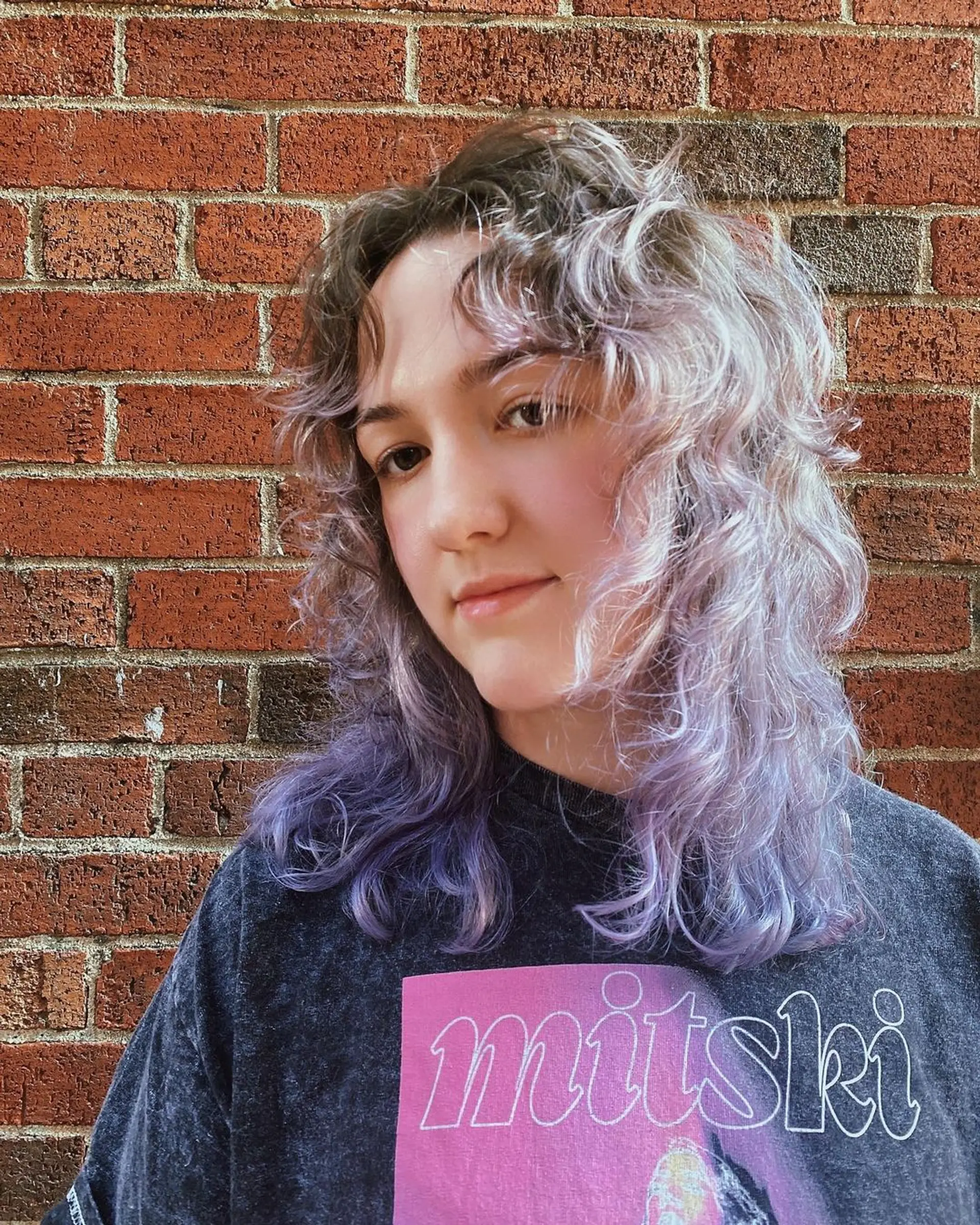 A wavy medium-length hairstyle with light brown roots blending into pastel purple, featuring layered waves and fringe bangs by Coco. 1