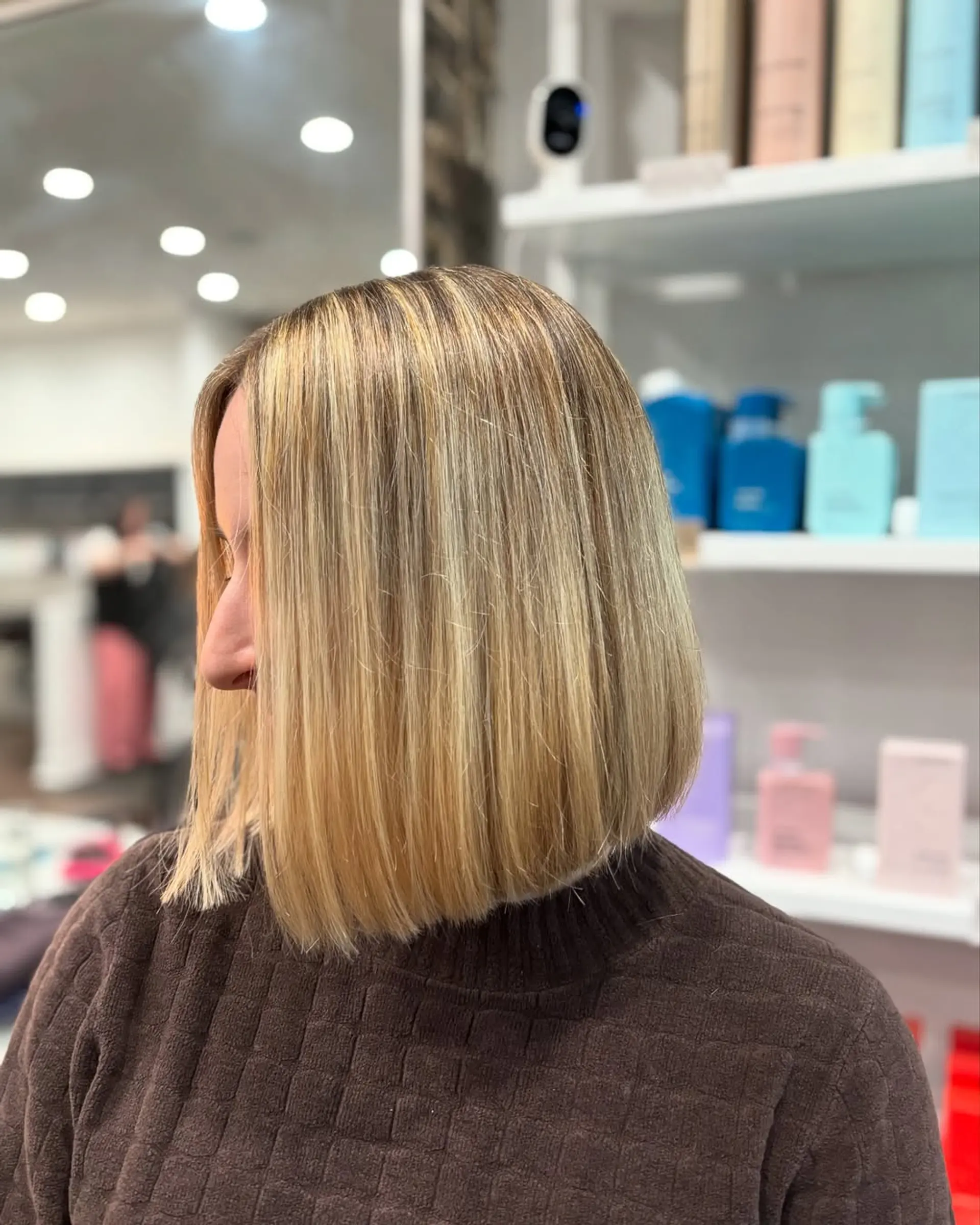 A sharp, modern blunt bob falling just above the shoulders, characterized by its precise, clean lines and a smooth, straight style, complemented by subtle dimensional blonde highlights for added depth and brightness. 1