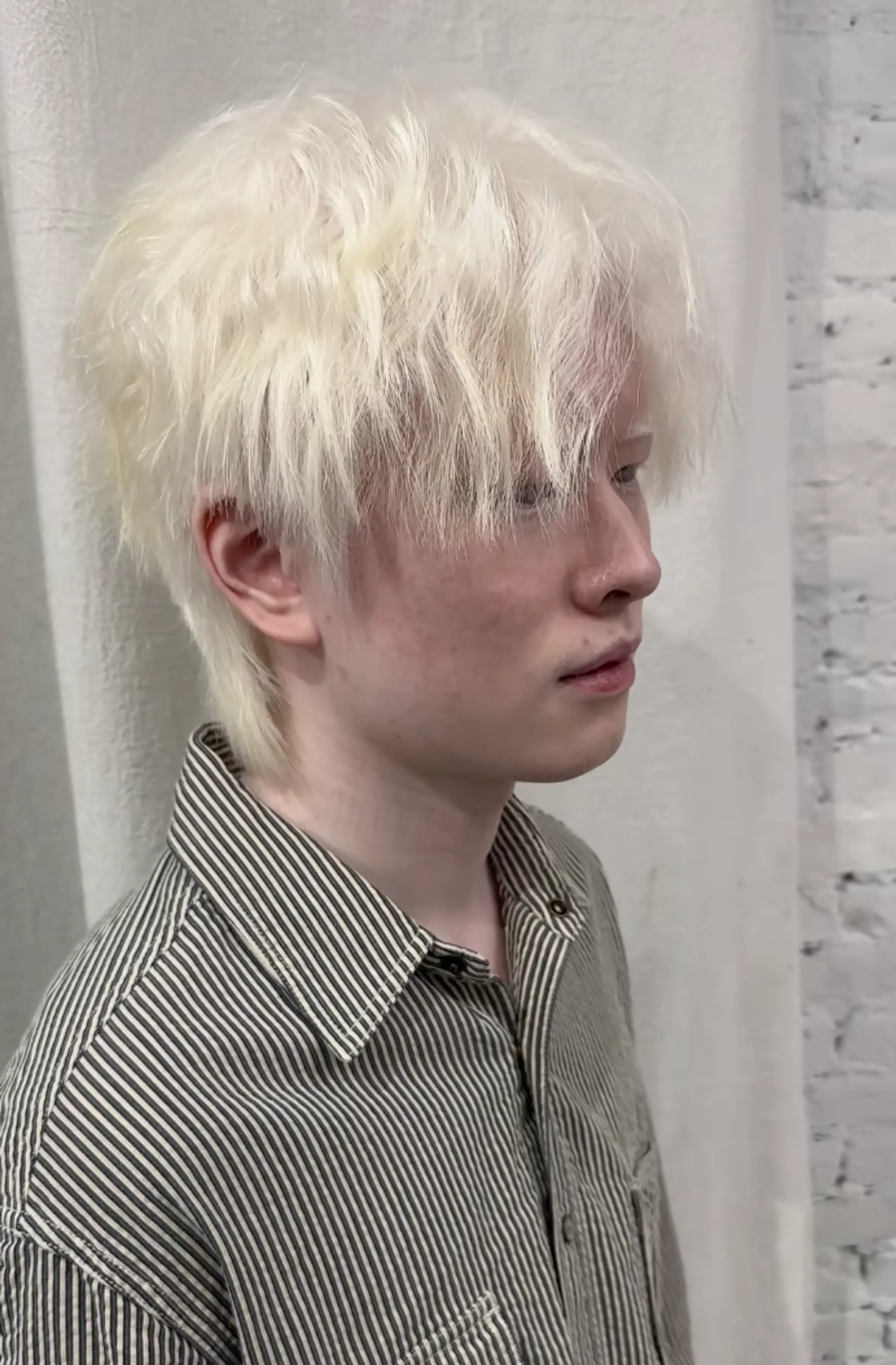A tousled, medium-length wavy hairstyle with a textured fringe, feathered ends, and a striking platinum blonde color. 1