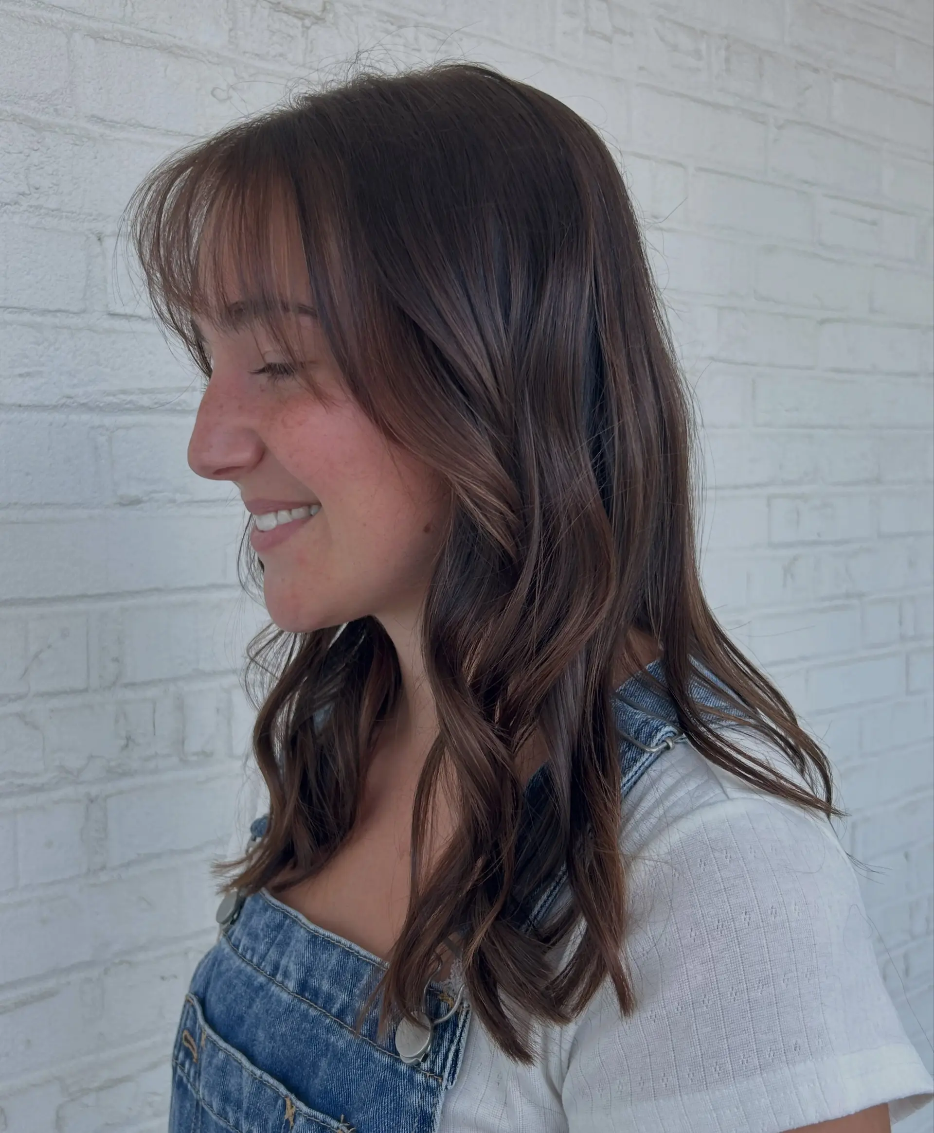 Subtle lived-in brunette balayage styled into loose, gentle waves and paired with soft, wispy bangs. 1