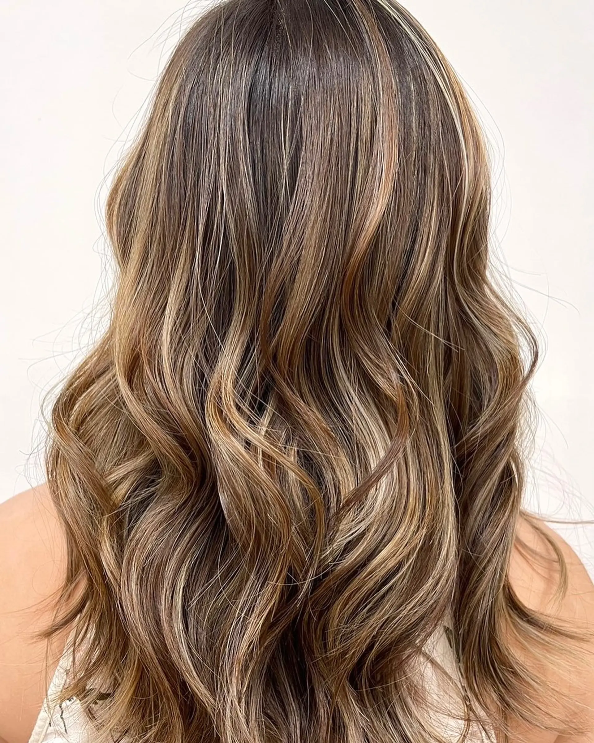 Long brunette hair styled in soft waves with dimensional honey blonde and caramel highlights throughout. 1