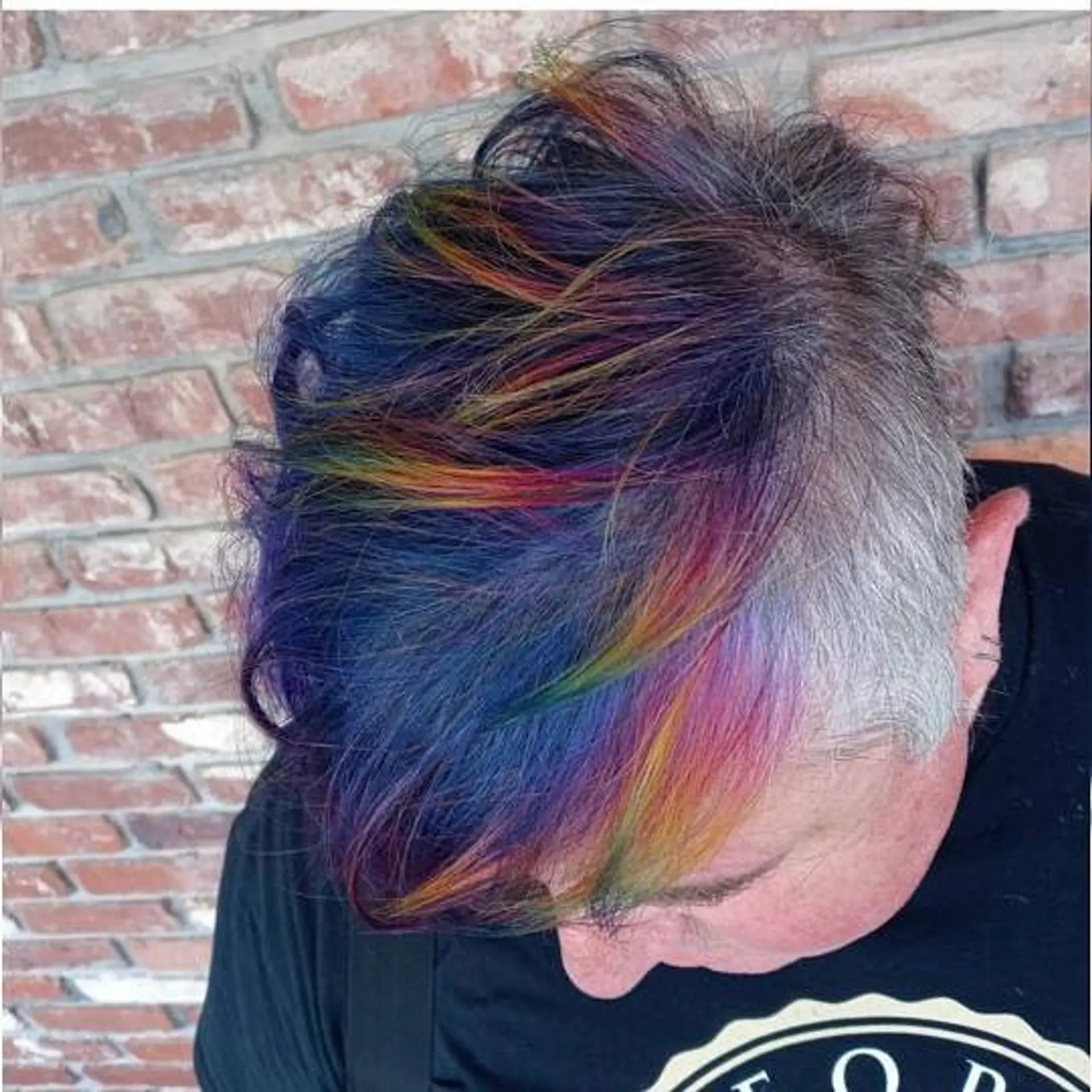 A short undercut pixie featuring closely cropped natural grey sides with vibrant, multi-tonal rainbow colors swept across the textured top. 1