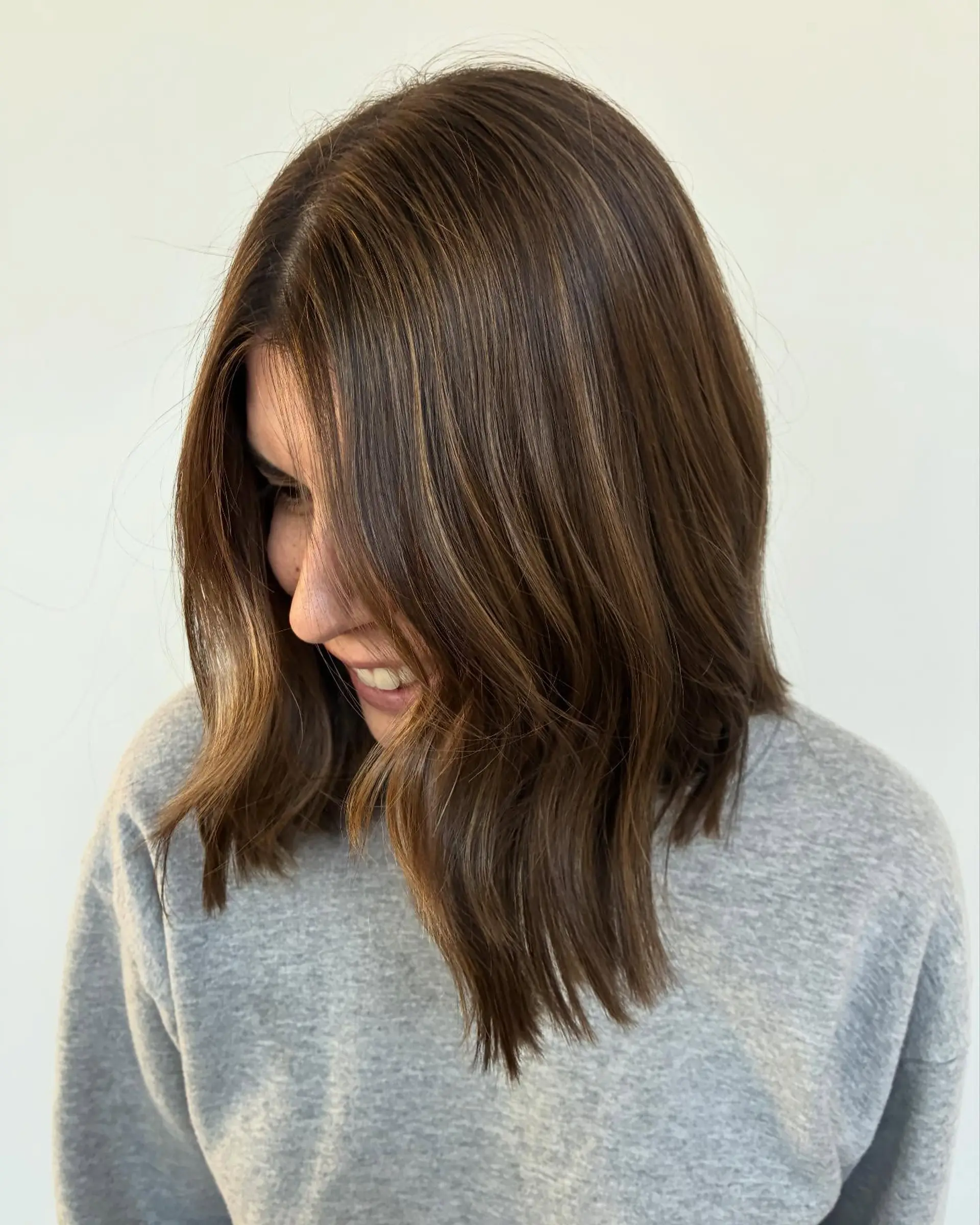 A collarbone-length layered lob featuring subtle warm brown highlights and a soft, natural bend. 1