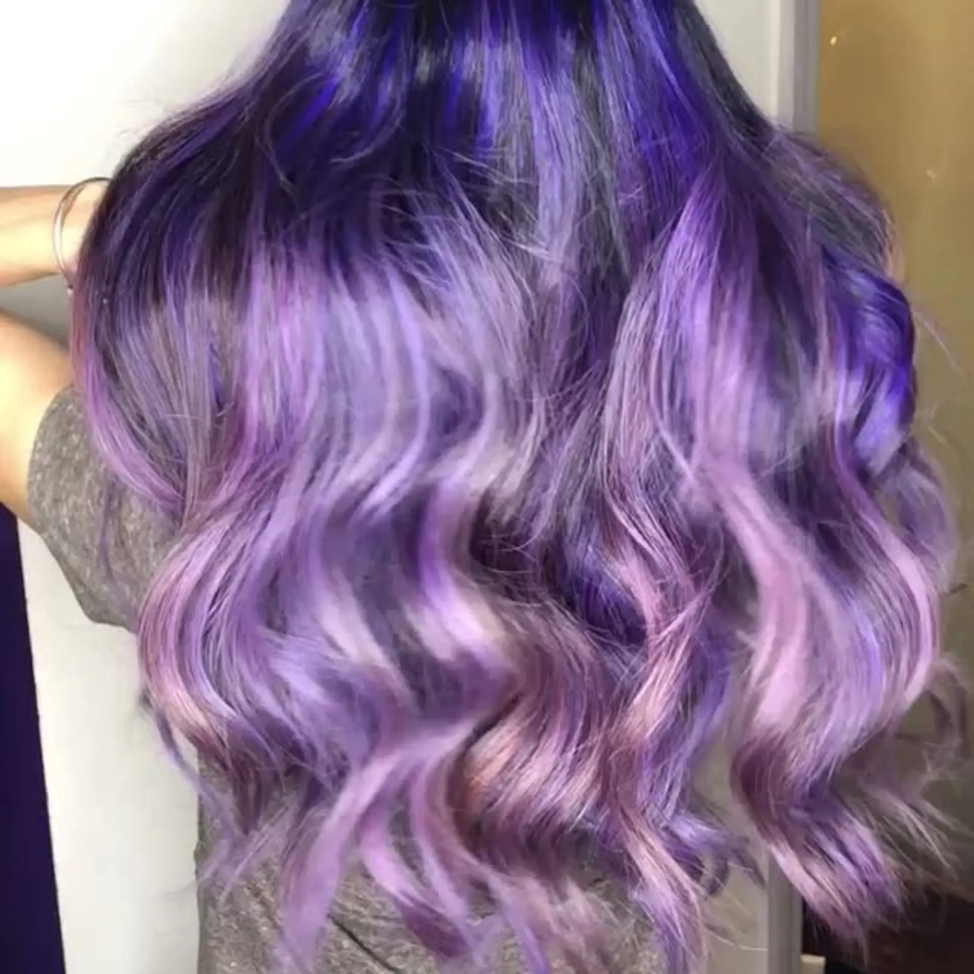 Long wavy hairstyle featuring deep violet roots melting into vibrant purple and soft pastel lavender ends. 1