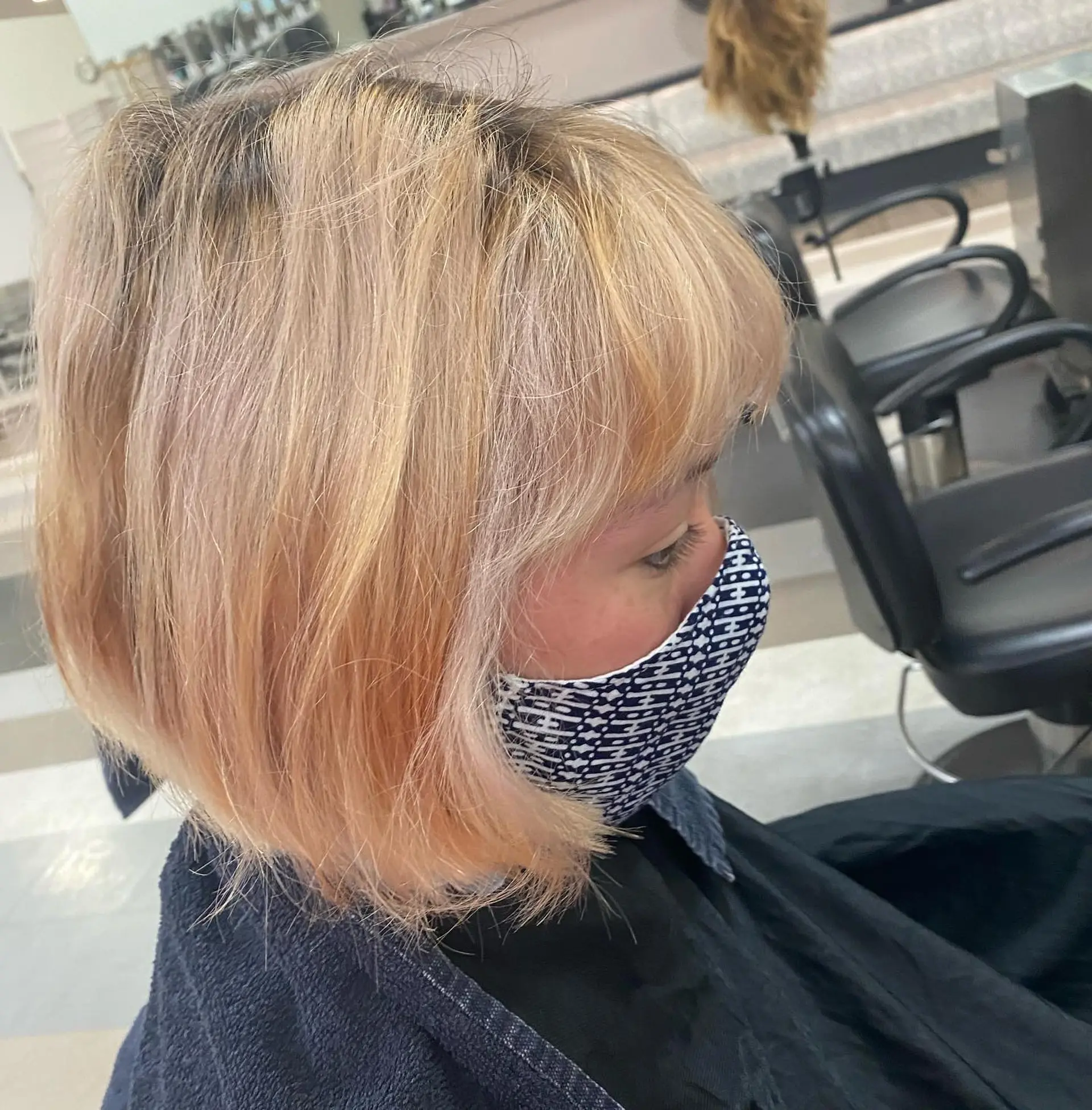 A textured chin-length French bob featuring full eyebrow-skimming bangs in a soft peach-toned light blonde. 1