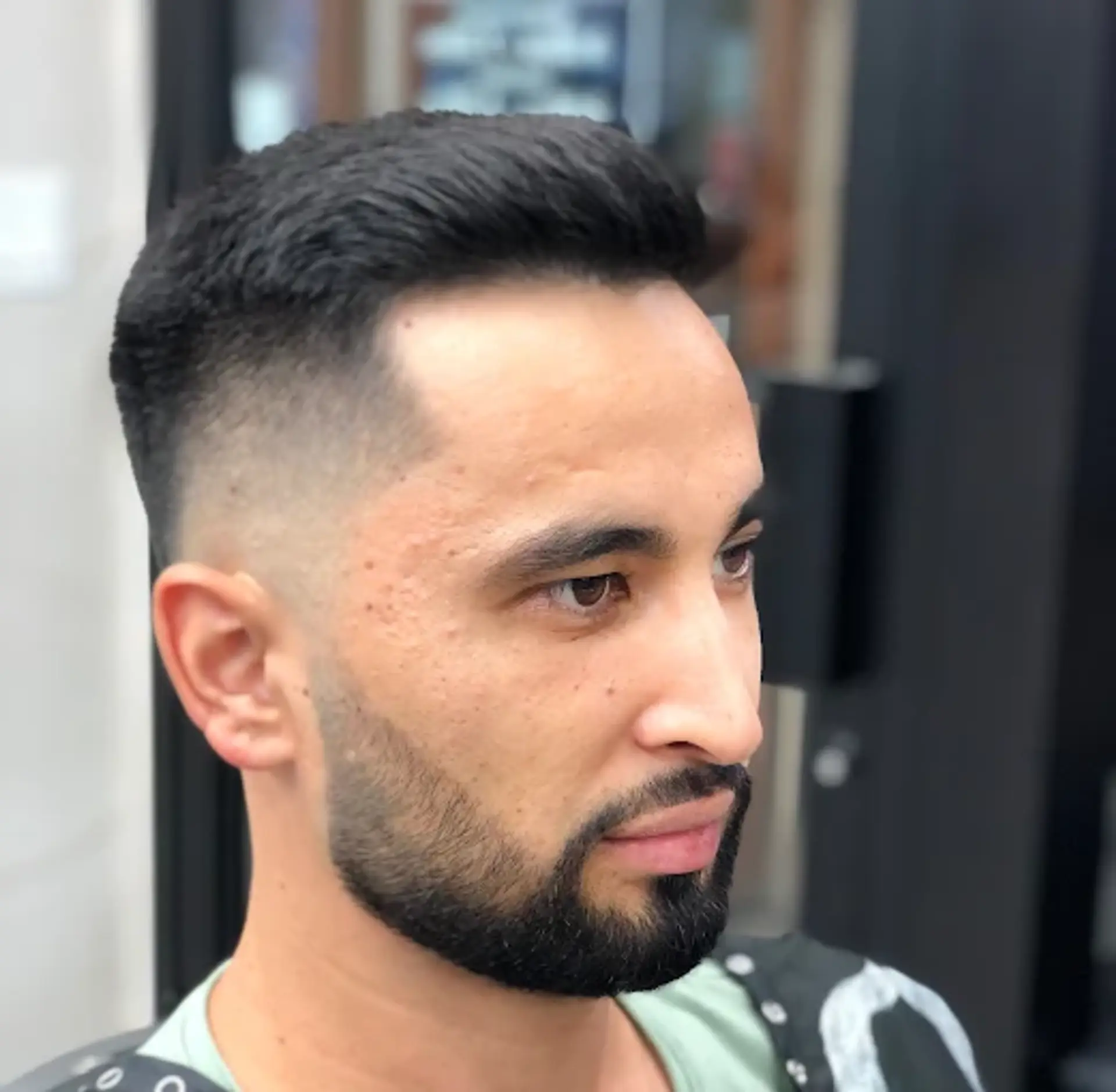 A sharp high skin fade on the sides and back combined with a textured, medium-length quiff styled upwards on top, creating a modern and clean aesthetic. 1