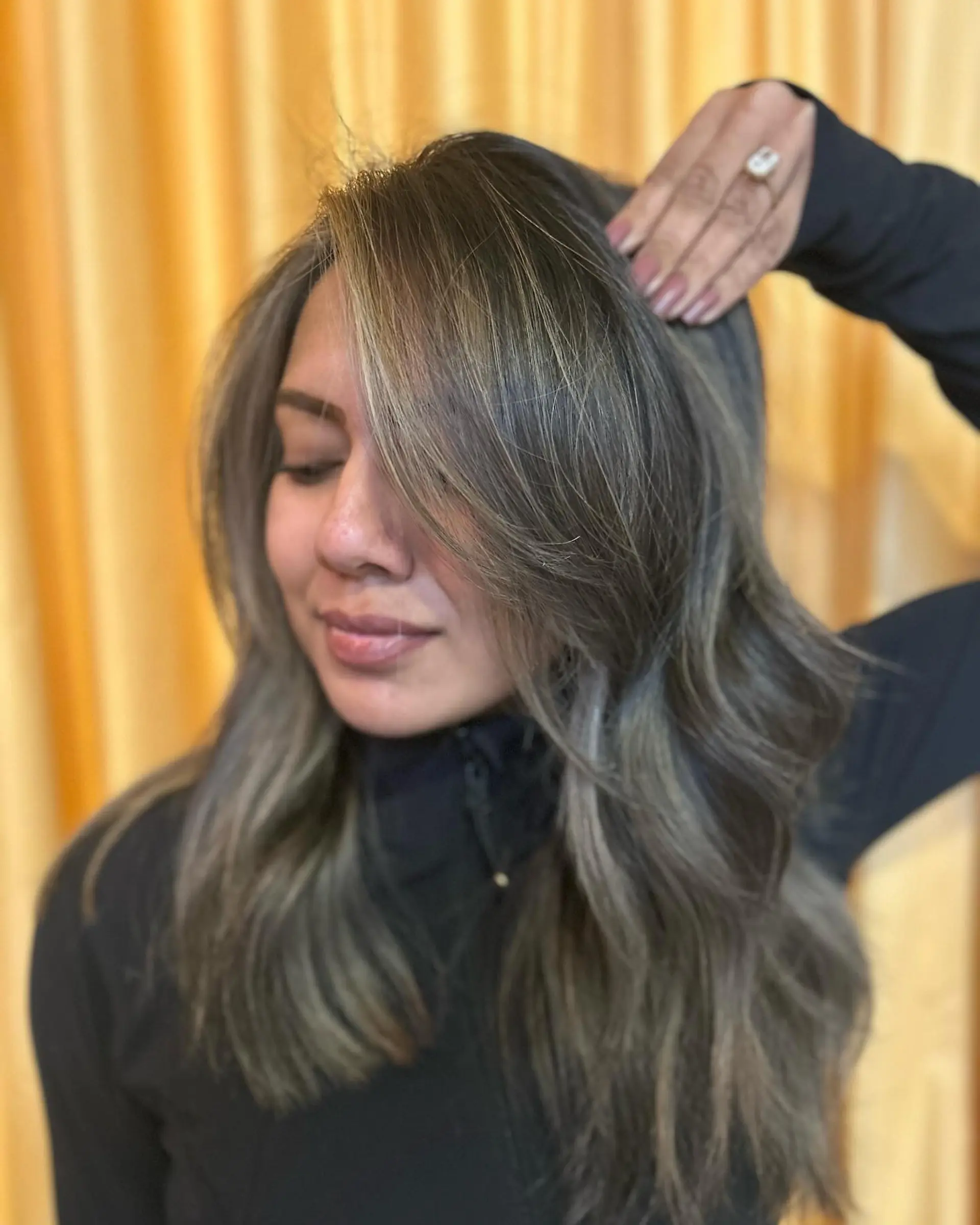 Cool-toned mushroom bronde balayage styled in soft, loose waves with face-framing fringe. 1