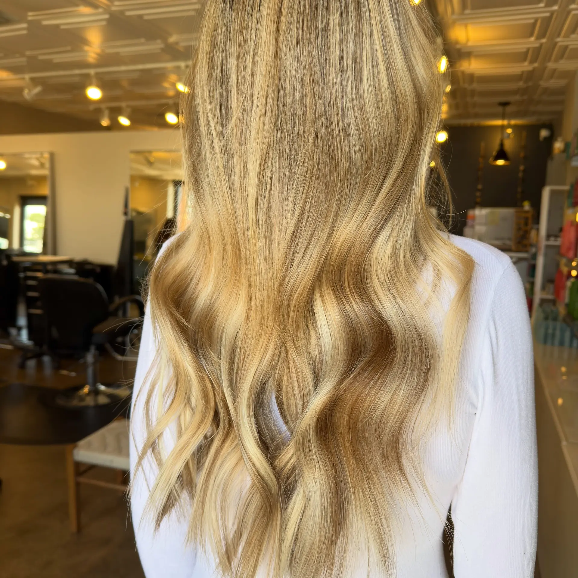 Long, dimensional golden blonde hair featuring seamless weft extensions styled into soft, flowing waves. 1