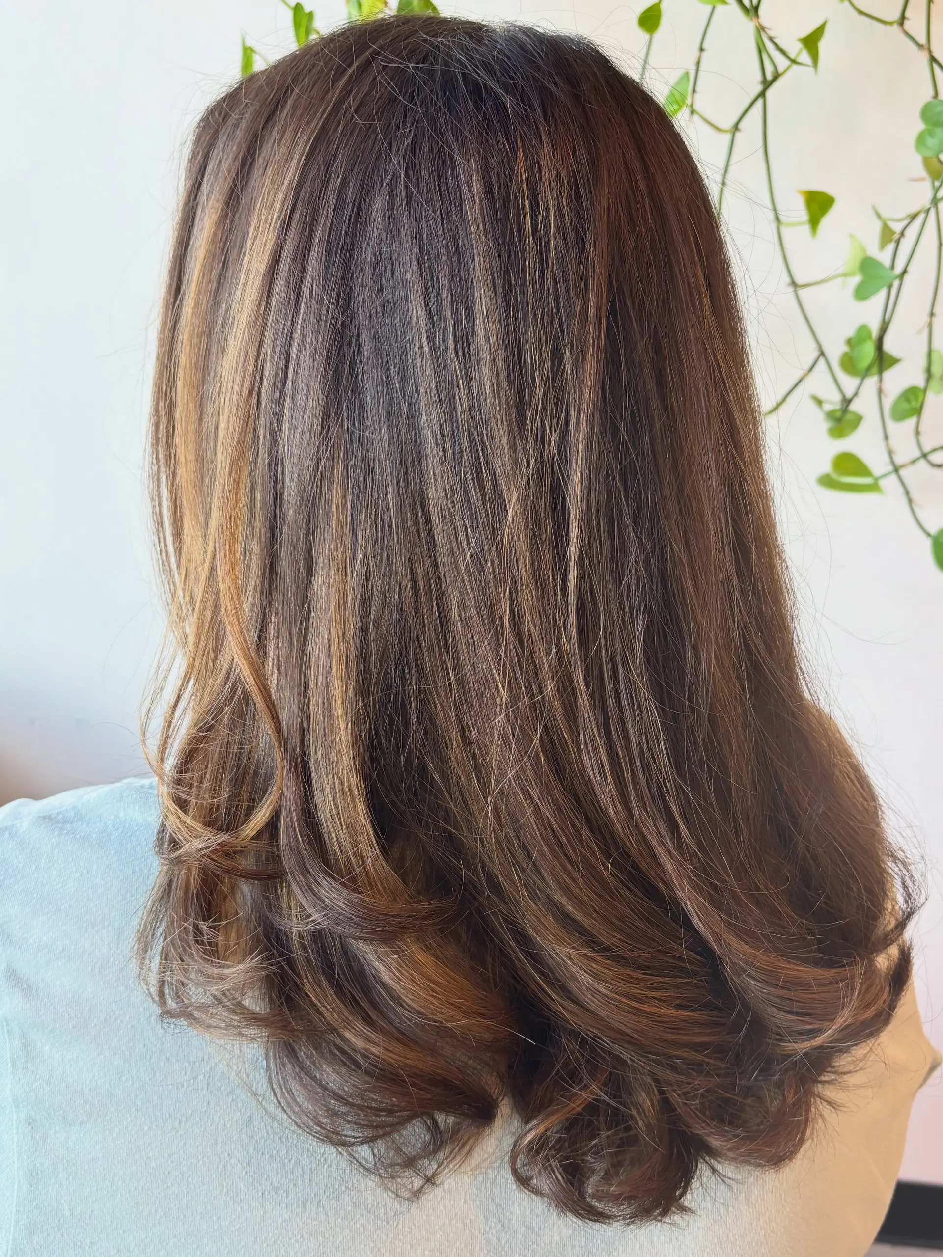 Medium-to-long layered brunette hair featuring subtle warm caramel highlights and softly curled under ends. 1