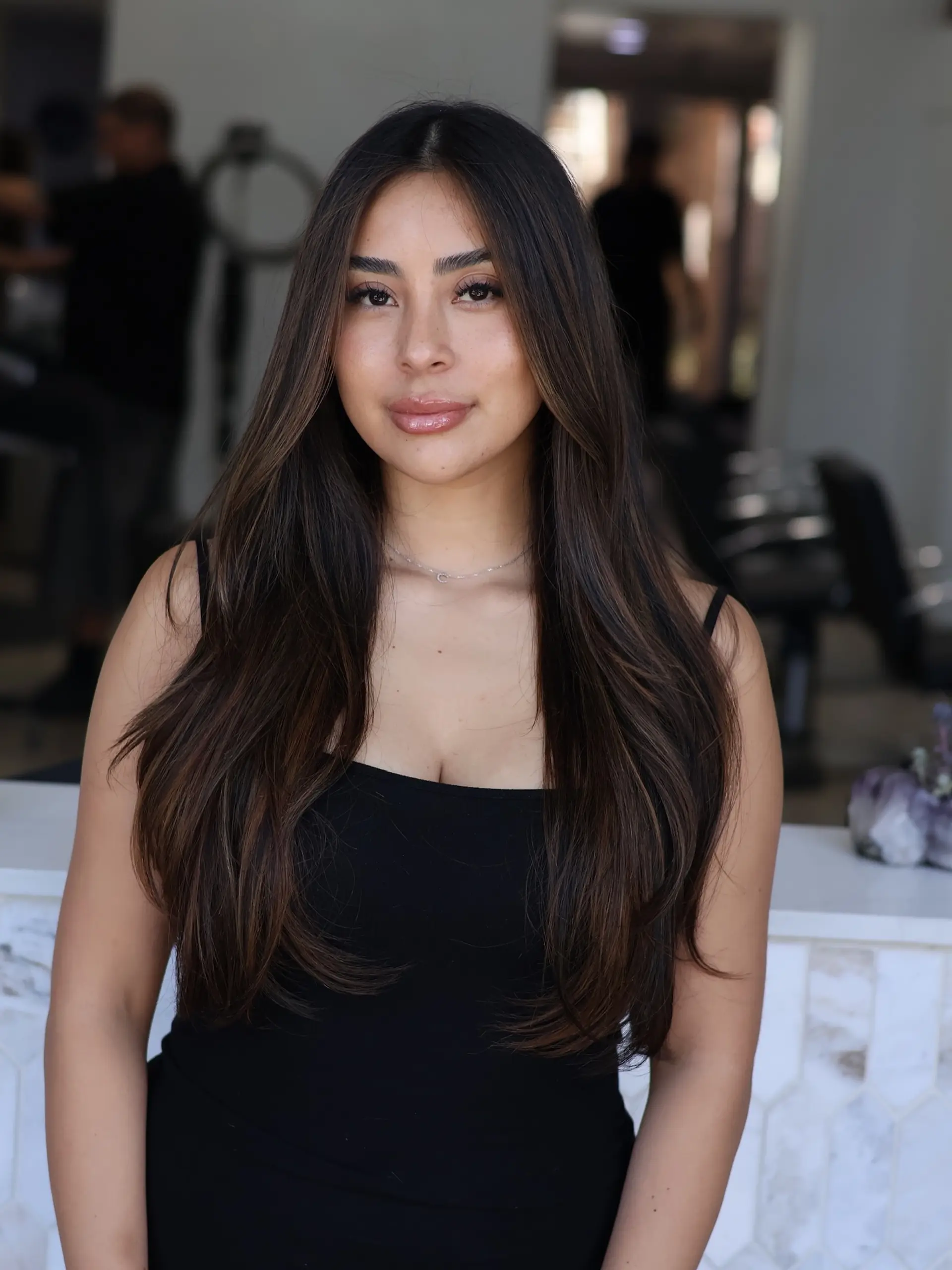 Long brunette hair with subtle caramel highlights styled in a smooth, polished blowout. 1
