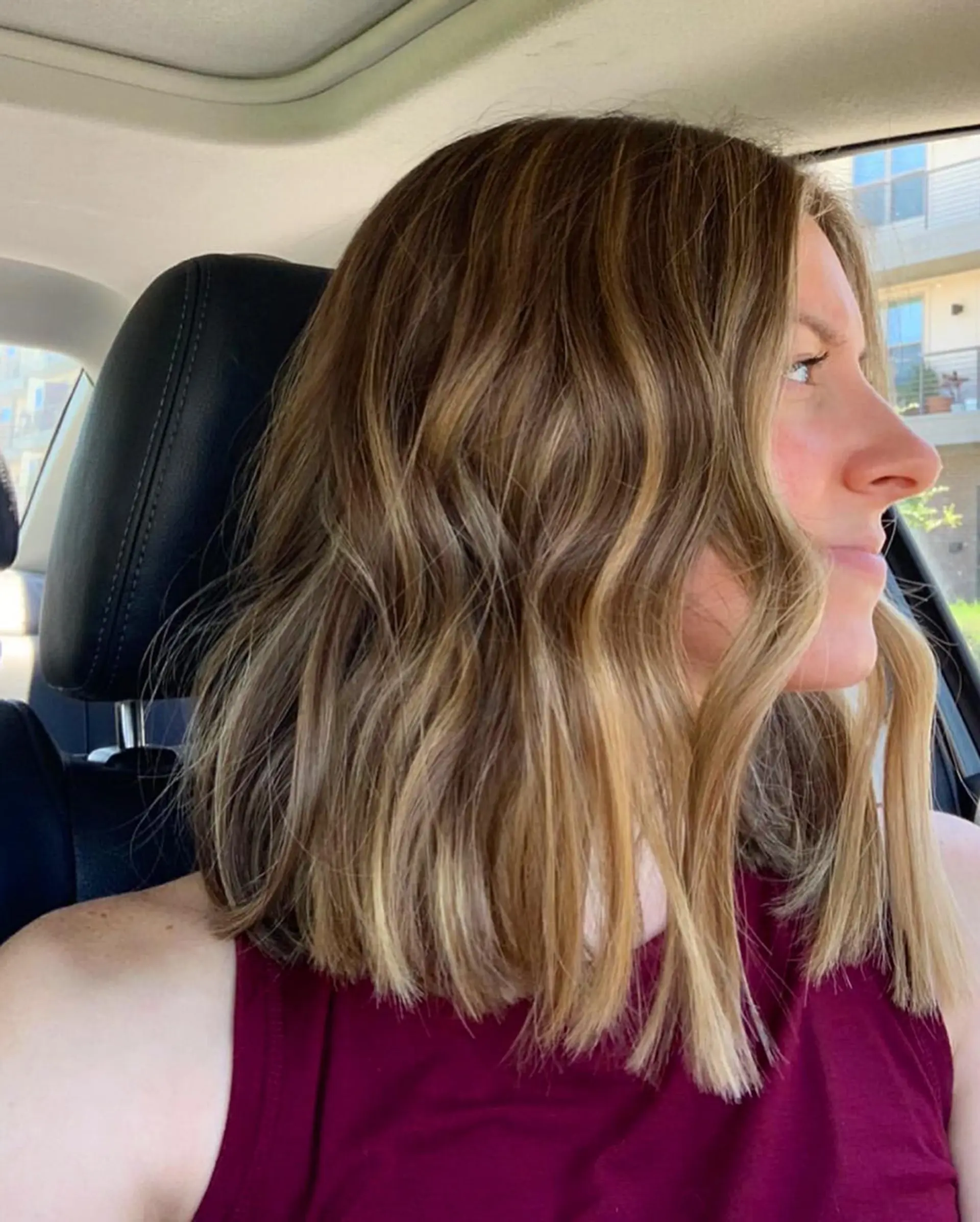 A collarbone-length blunt lob featuring warm dimensional blonde balayage highlights styled in loose, textured beach waves. 1