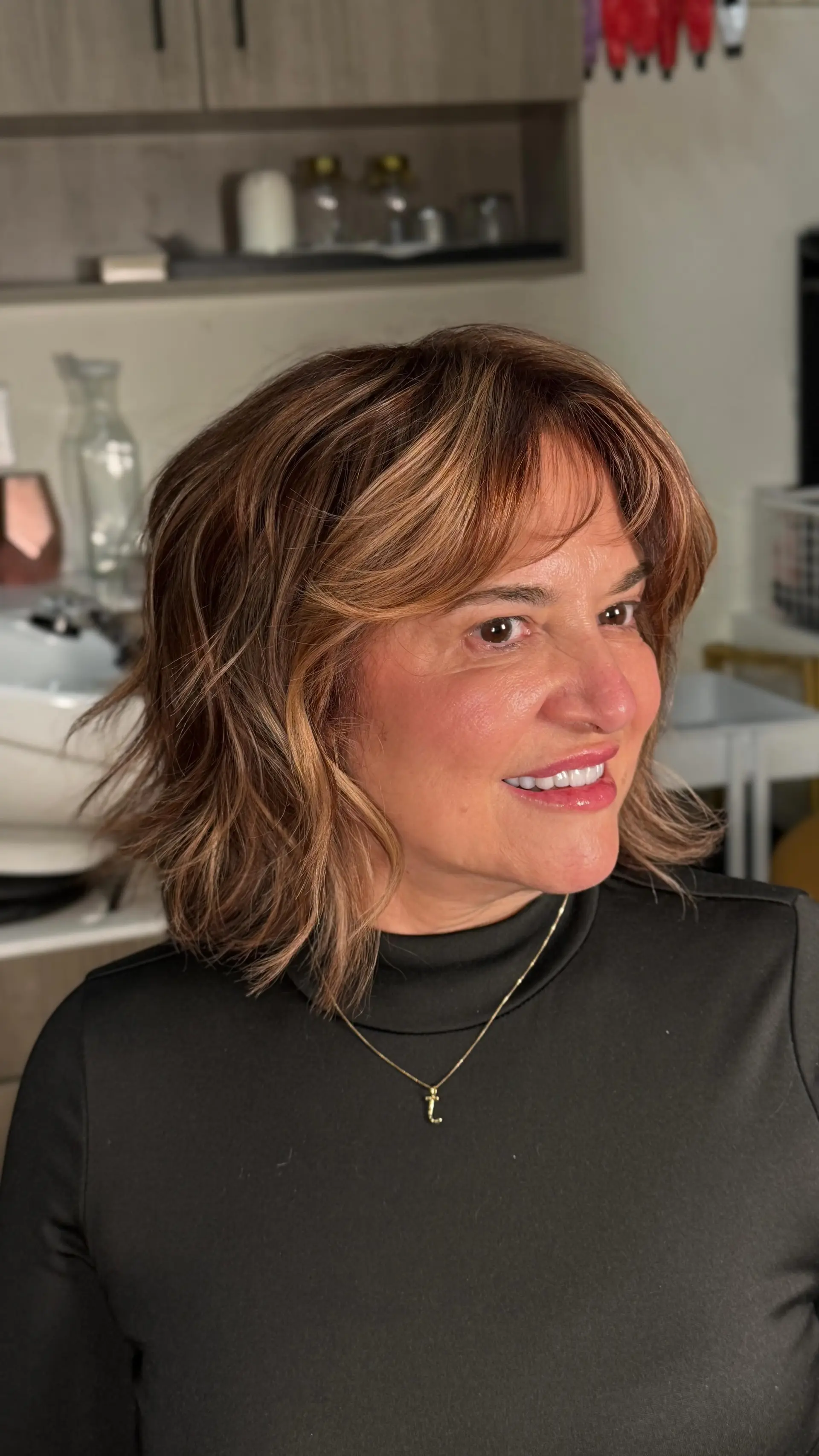 A textured layered shoulder-length bob styled with soft, piecey curtain bangs and warm caramel dimensional highlights. 1