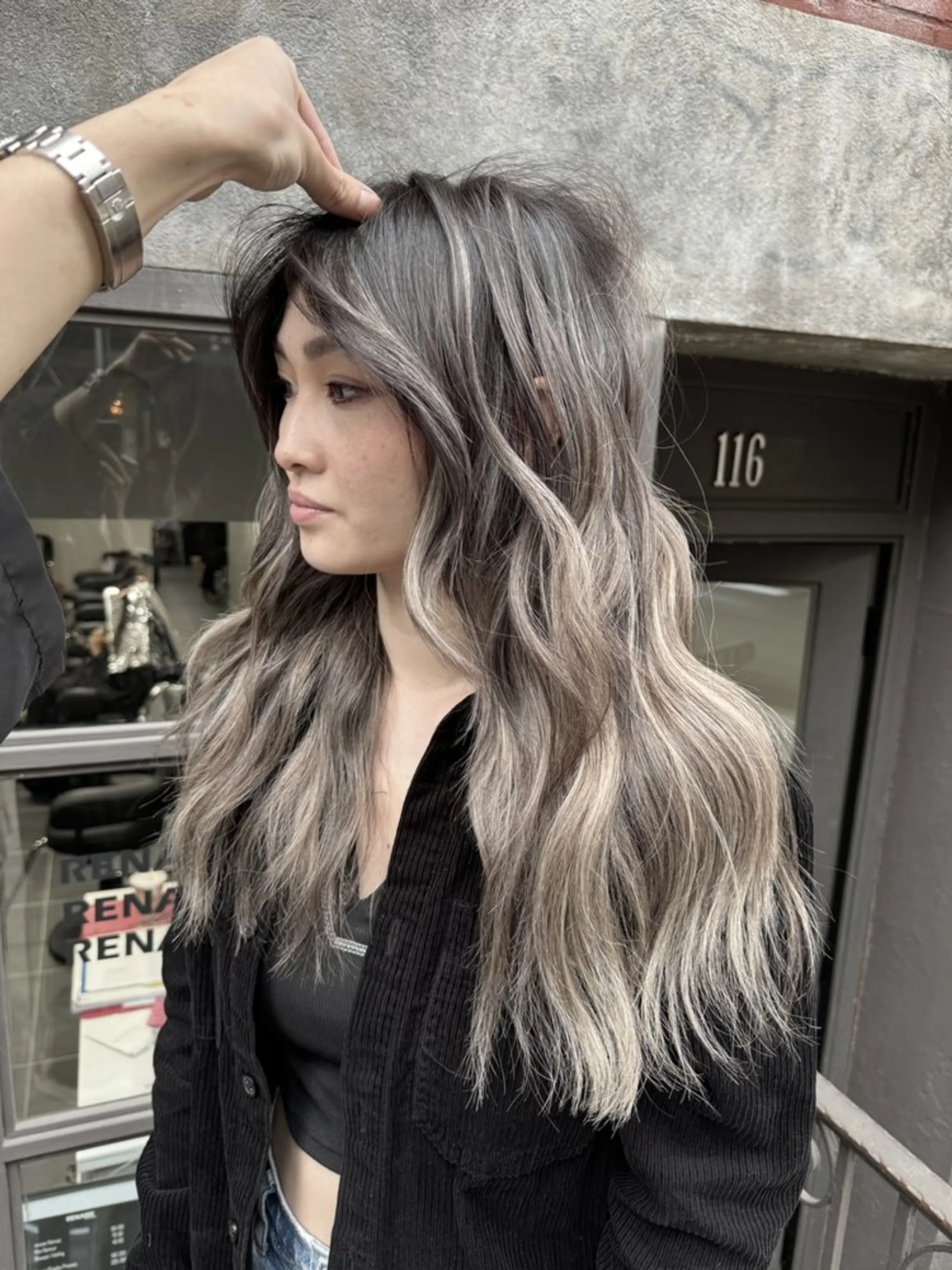 Long, wavy hair with ash brown base color, silver, and blonde highlights in an ombre effect. Layered cut adds volume and movement.