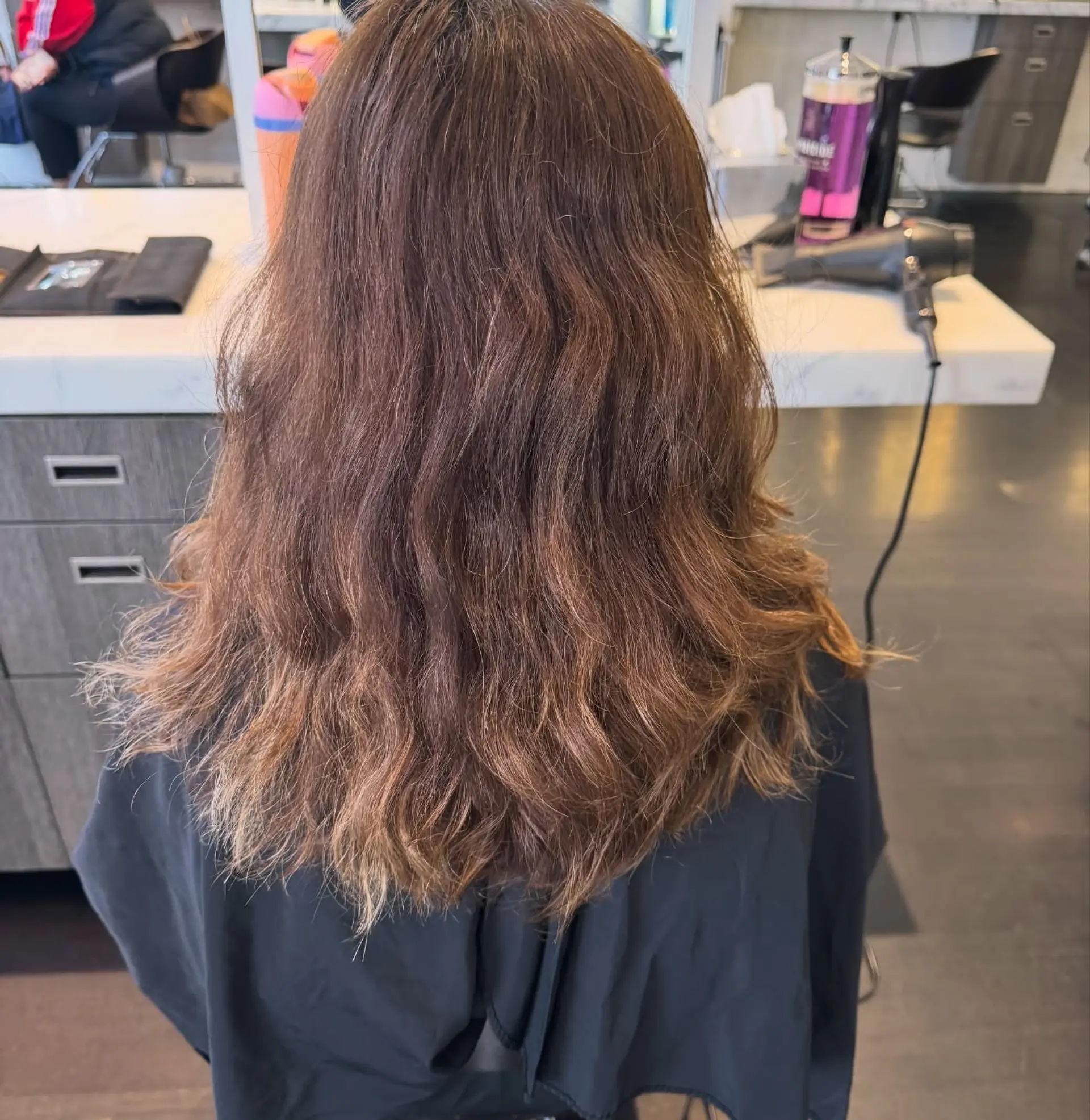 Medium-length brunette hair styled with soft, natural waves and subtle warm golden highlights. 1