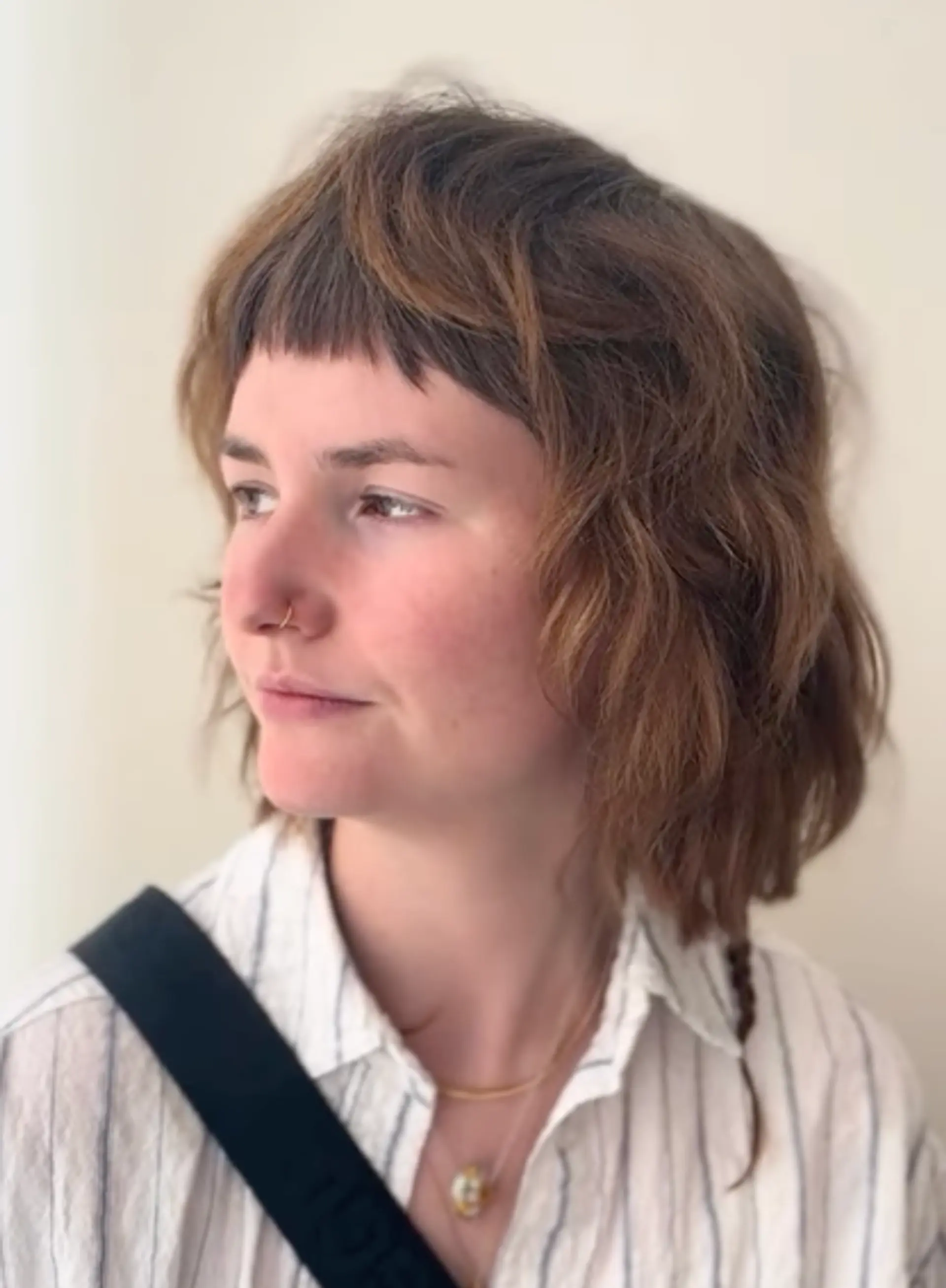 A wavy, medium-length hairstyle with brown and auburn tones, featuring choppy layers and short, edgy bangs, creating a natural, carefree look. 1