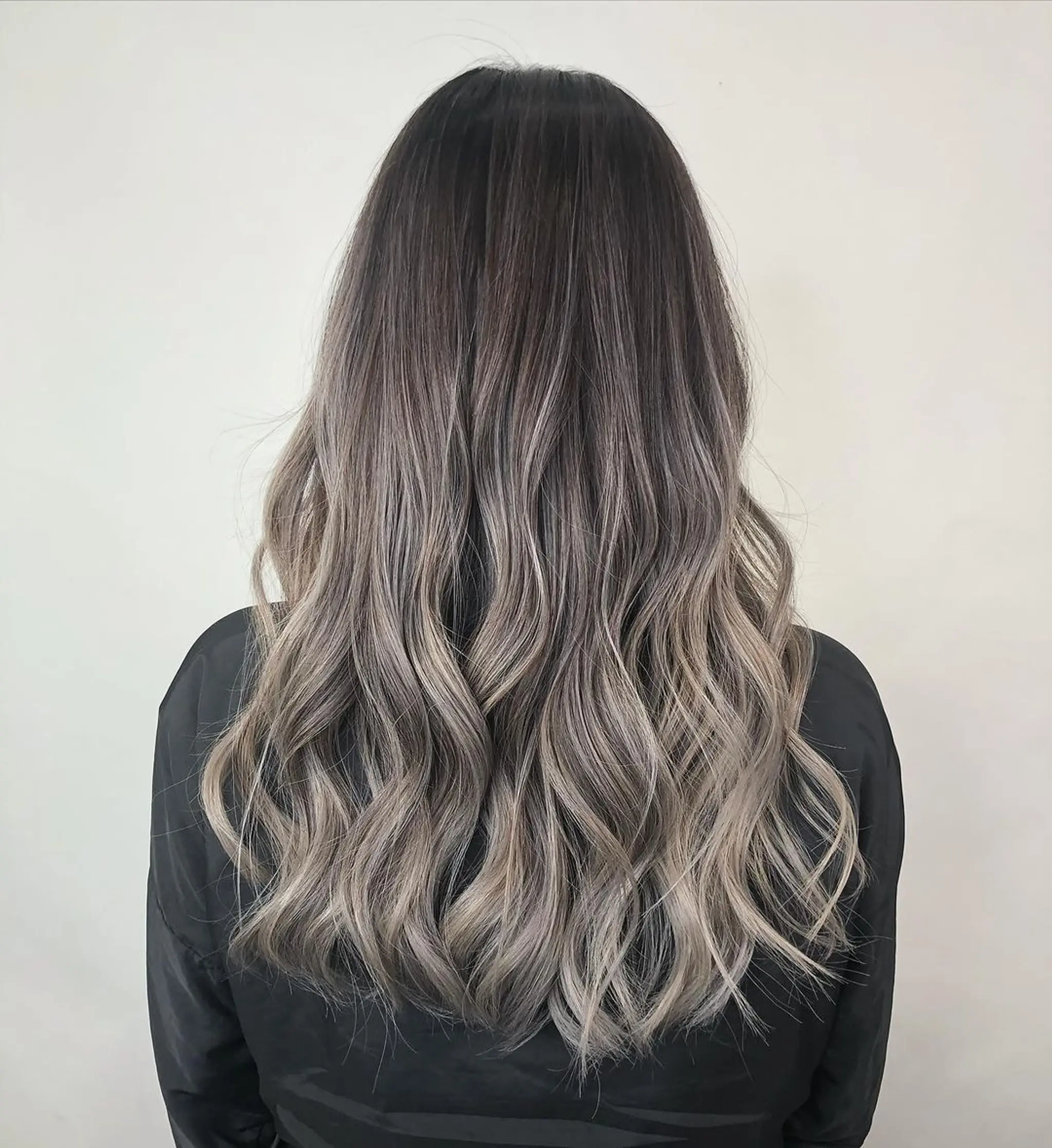 Long, wavy hair with dark brown roots transitioning to ash blonde and silver tones, featuring soft waves and an ombre effect.
Stylist - @xcellent_jason