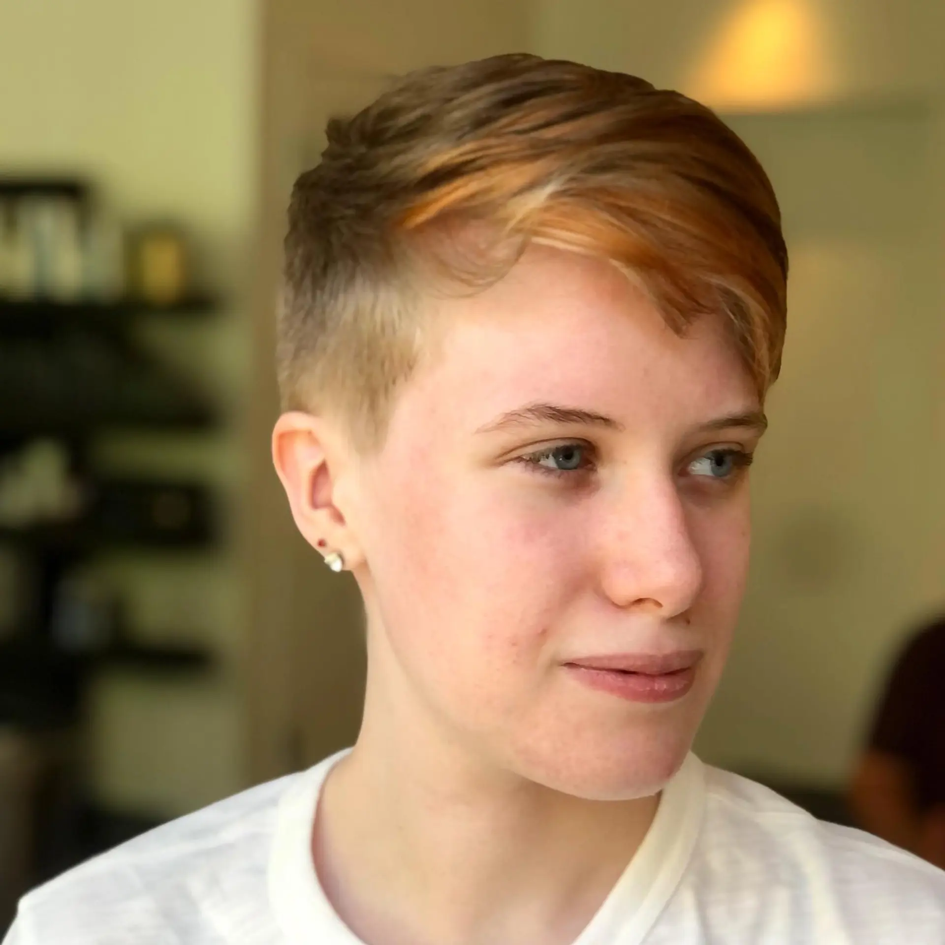 A tapered pixie undercut featuring clipped sides and a longer, side-swept top accented with warm copper highlights. 1