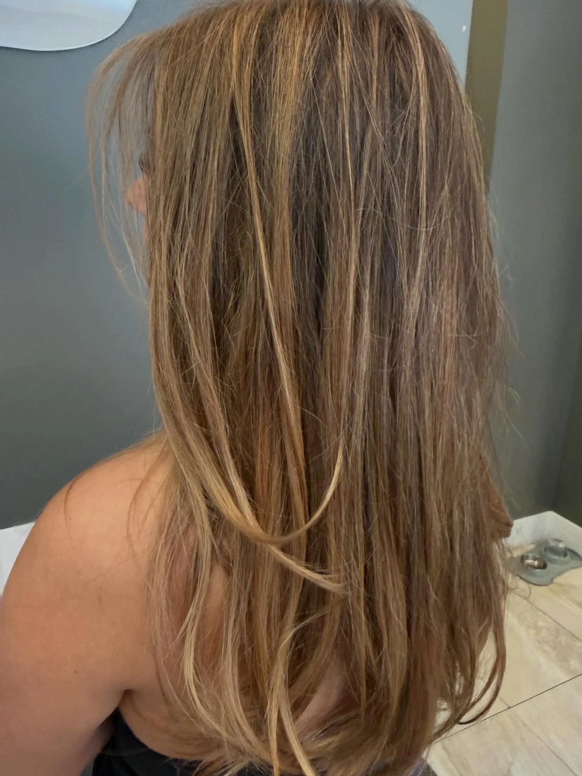 Long, naturally textured straight hair styled with warm honey and caramel highlights over a light brown base with soft face-framing layers. 1