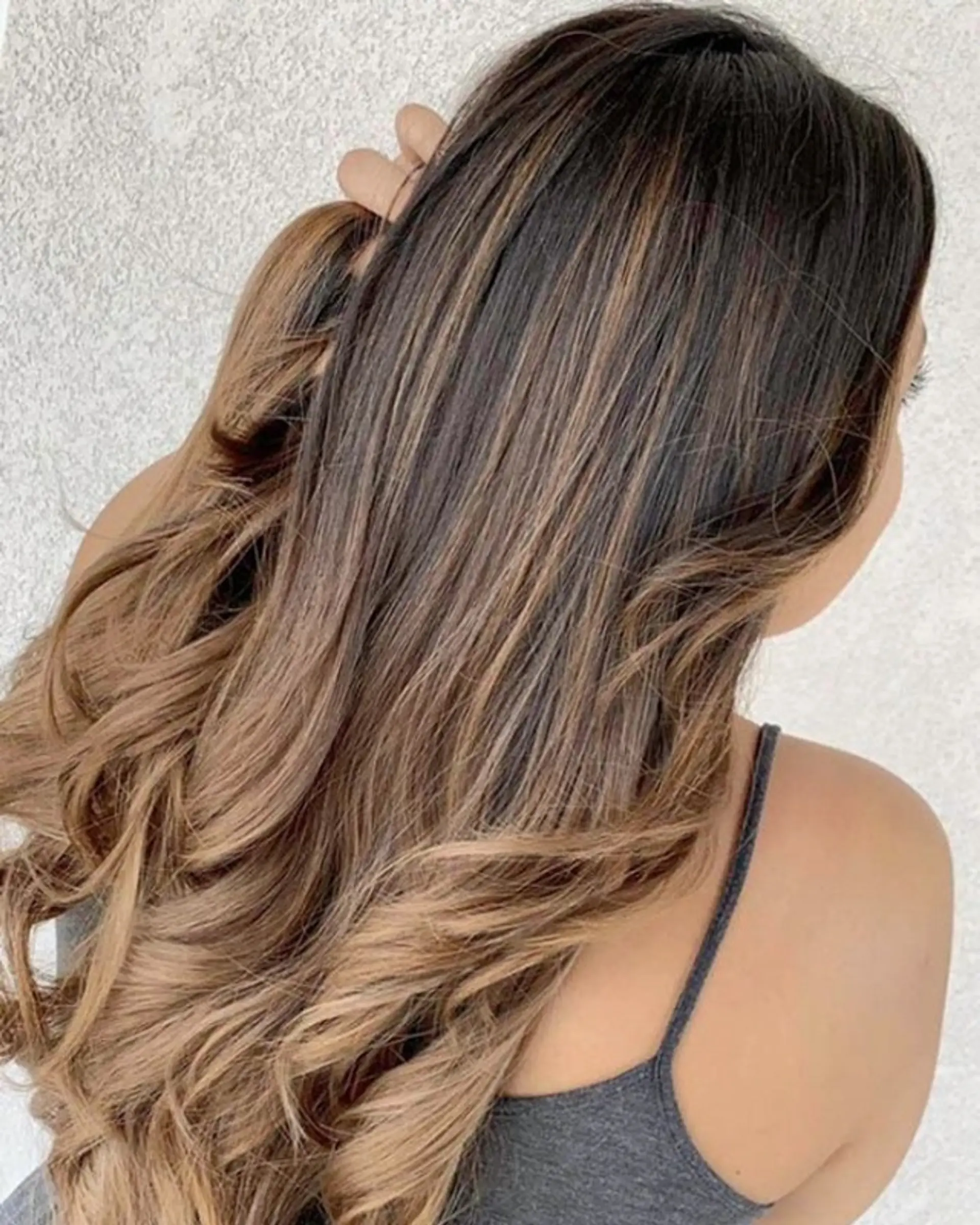 Long hair with a sophisticated balayage, blending dark brown roots into warm caramel and golden blonde mid-lengths and ends. The style is finished with soft, bouncy waves that add volume and movement. 1