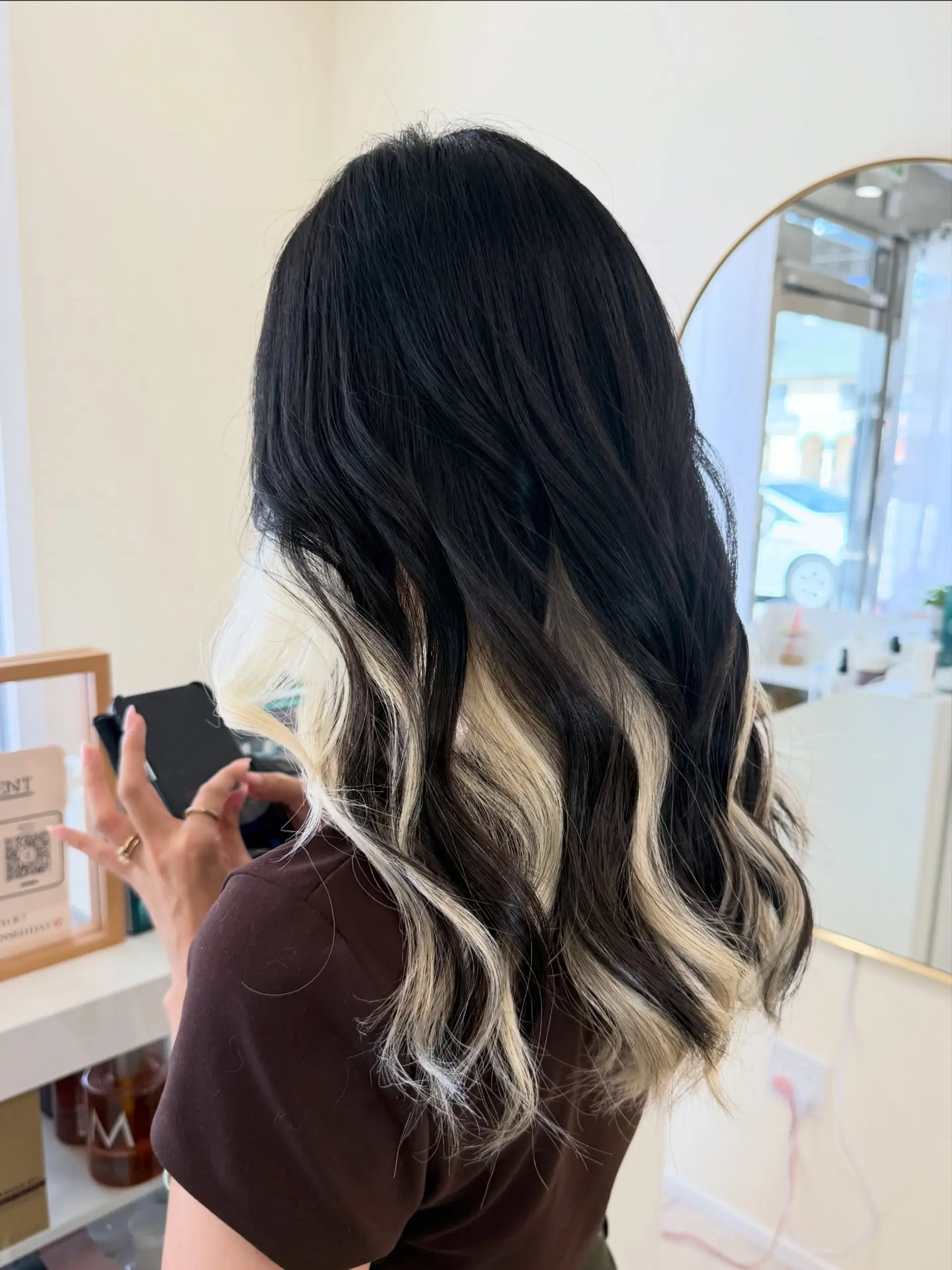 Long jet-black hair styled with soft waves, revealing high-contrast platinum blonde peekaboo underlights. 1