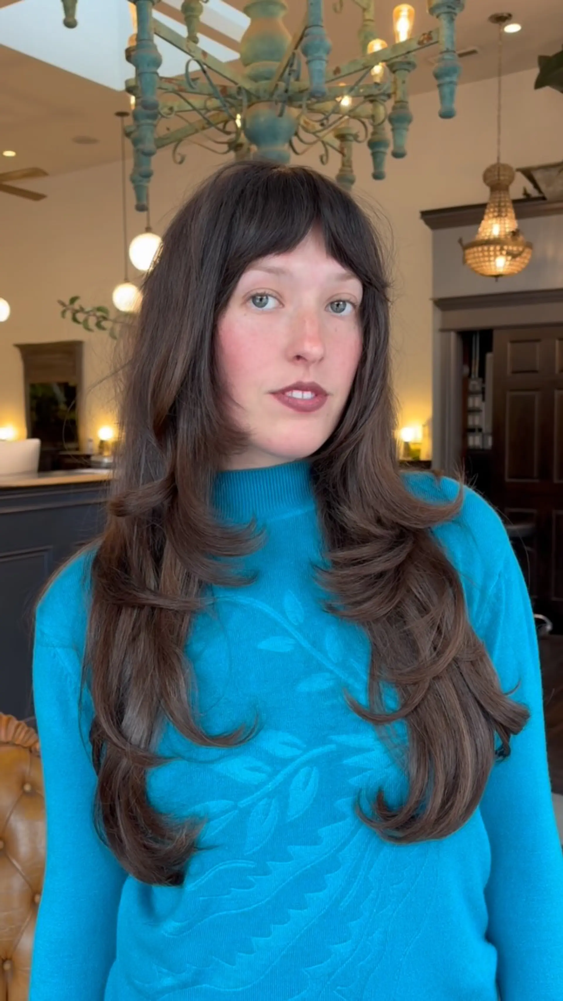 Long brown hair cut with tiered, face-framing layers and soft bangs, styled with flipped-out ends. 1