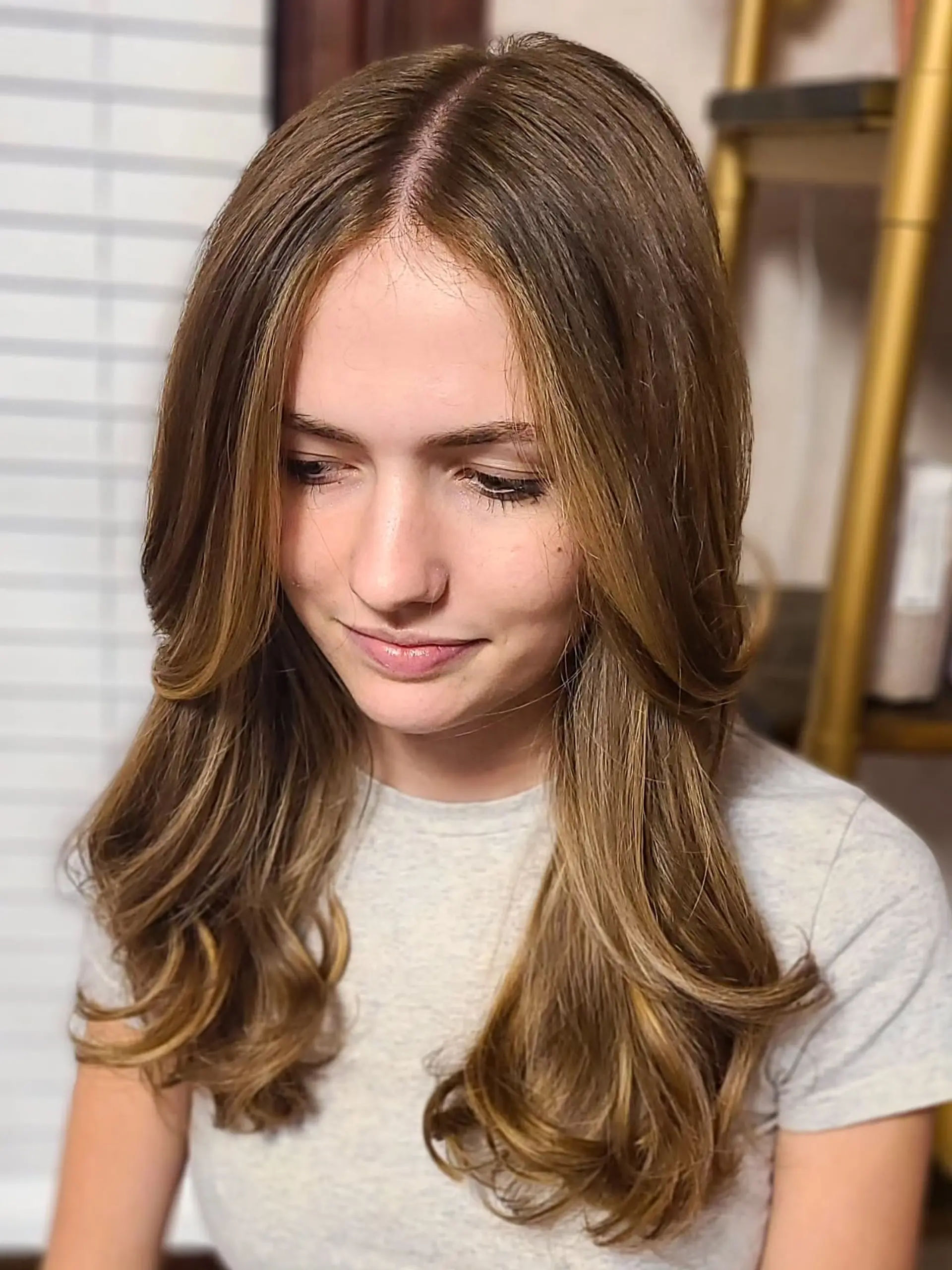 Long, wavy hair with a dimensional golden-brown color, featuring soft, flowing waves that add movement and volume. The color melts seamlessly from a darker root to brighter caramel blonde ends, creating a sun-kissed, lived-in effect. 2