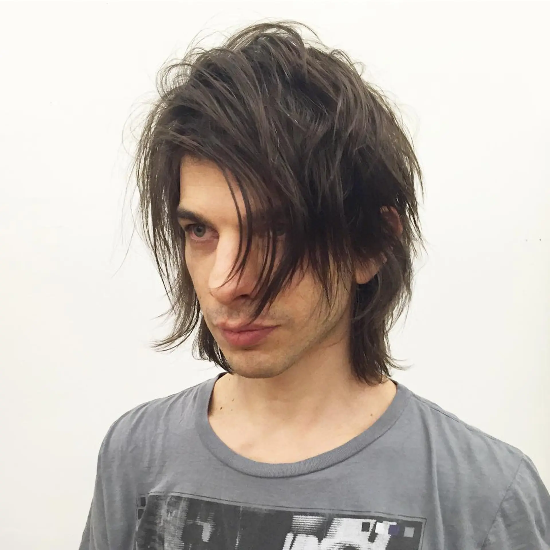 The hairstyle is medium-length and wavy with dark brown color, featuring tousled layers and a messy fringe for an edgy, rockstar look. 1