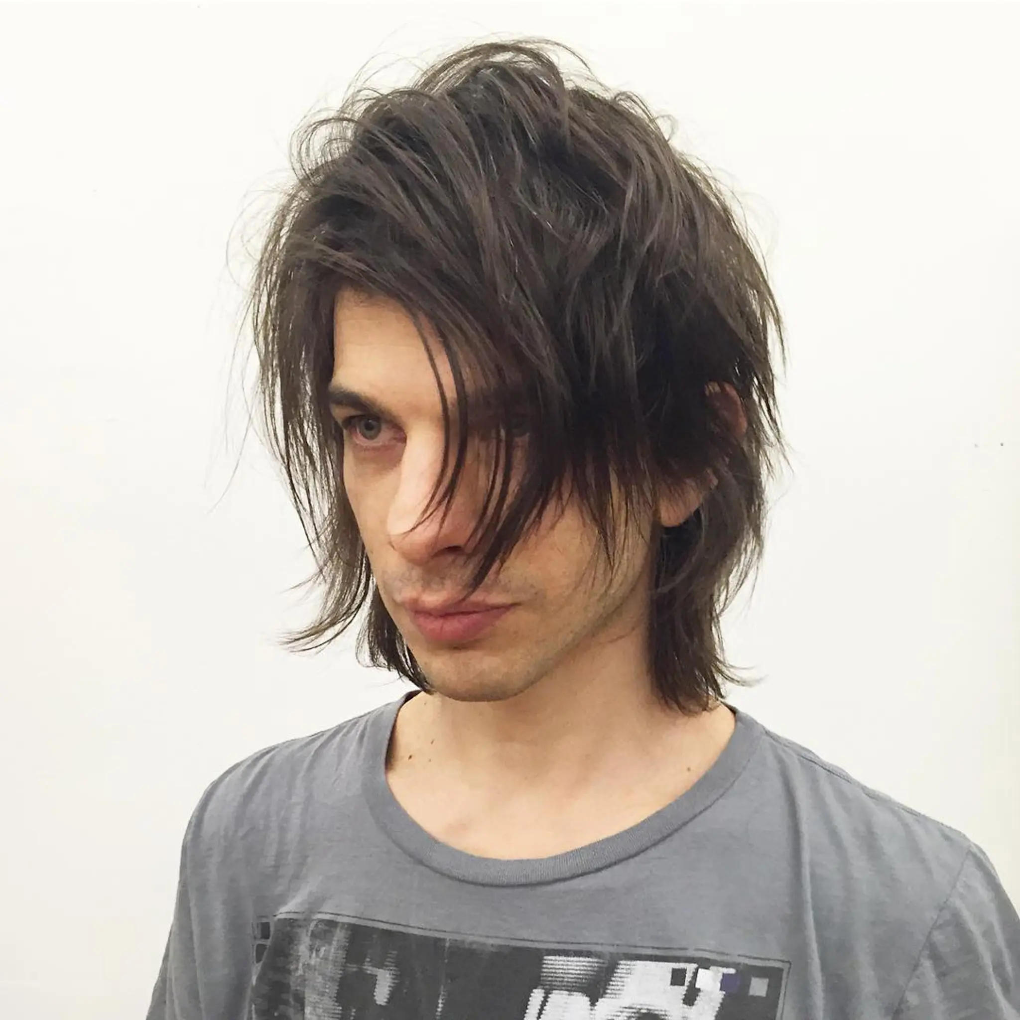 The hairstyle is medium-length and wavy with dark brown color, featuring tousled layers and a messy fringe for an edgy, rockstar look.