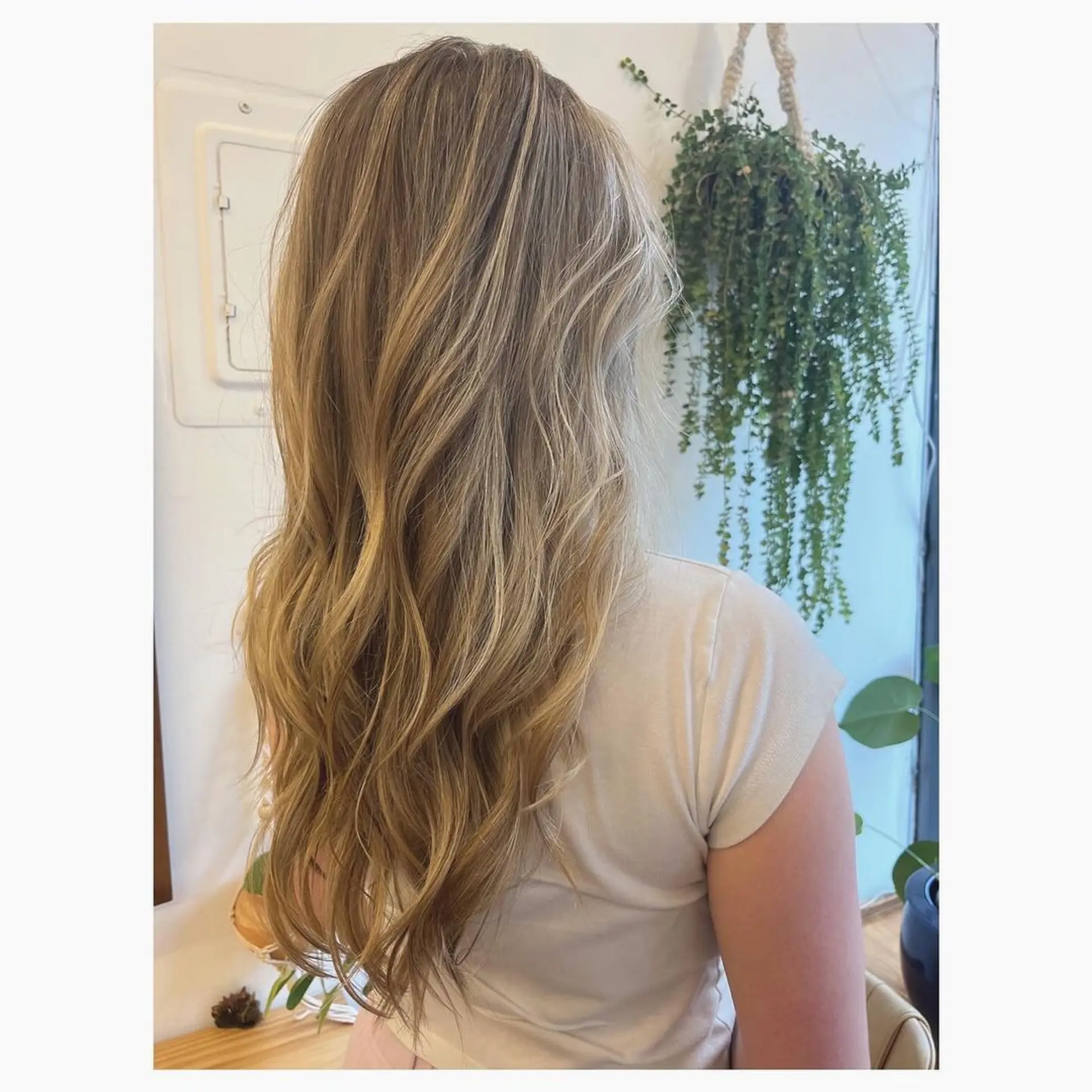 The hairstyle features long, layered waves with a soft texture and sunlit shine, blending honey blonde with golden highlights. 1