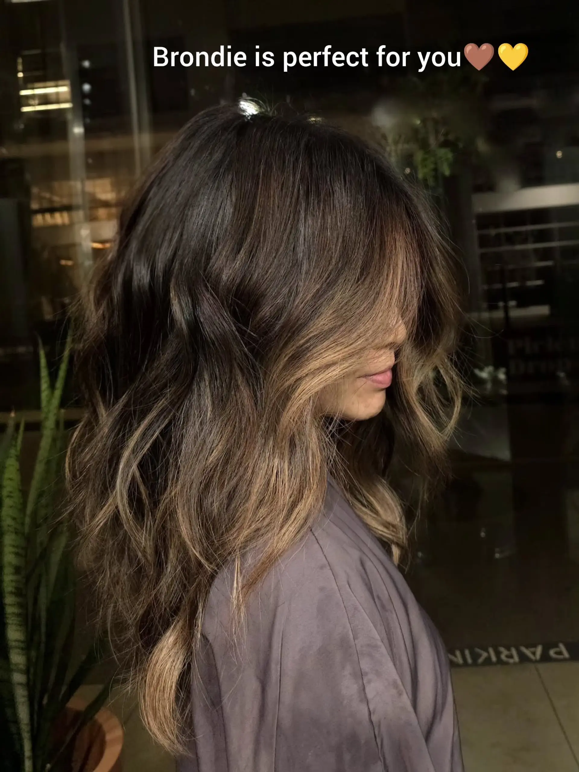 Long dark brown hair seamlessly blended with warm caramel and golden bronde balayage highlights, styled in loose soft waves with long face-framing layers. 1