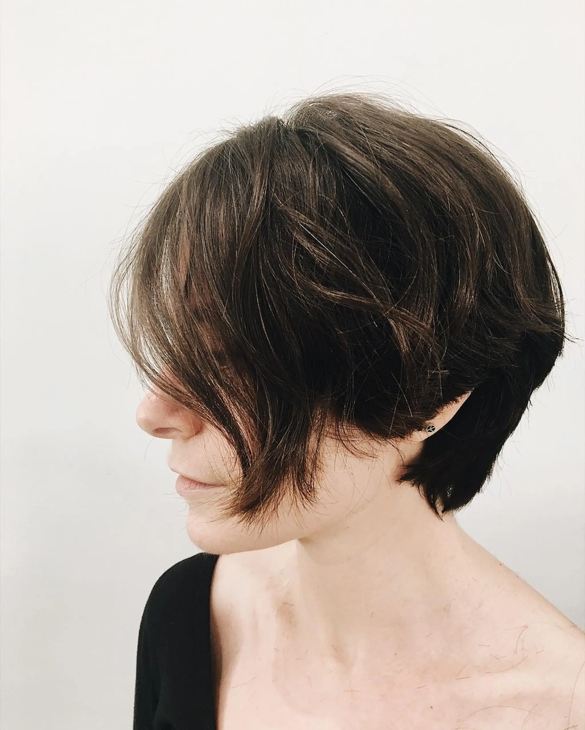 Short, dark brown, wavy bob with asymmetrical cut, side-swept bangs, and layered waves.