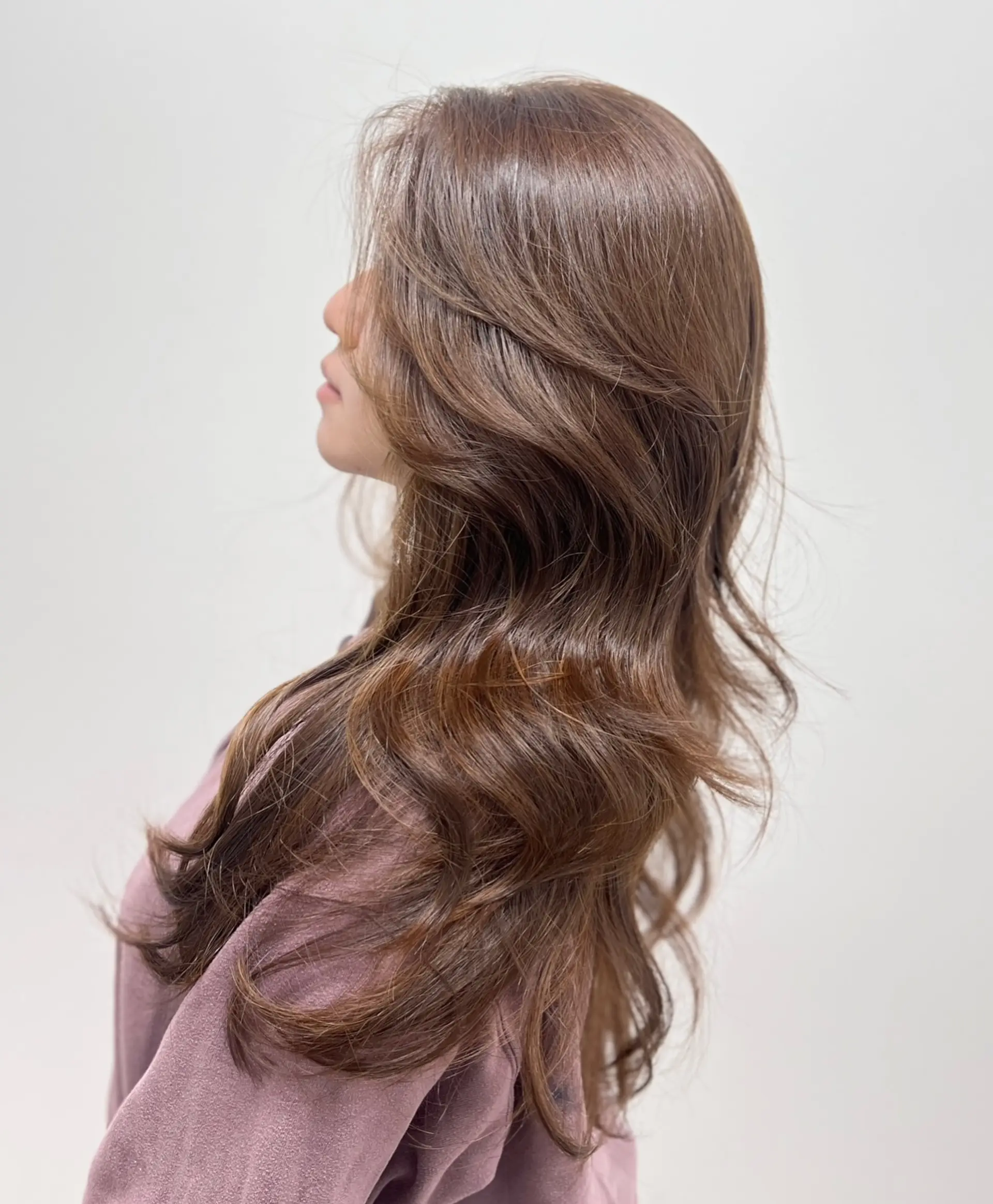 Long, glossy light brown hair styled in soft, bouncy waves with face-framing layers. 1