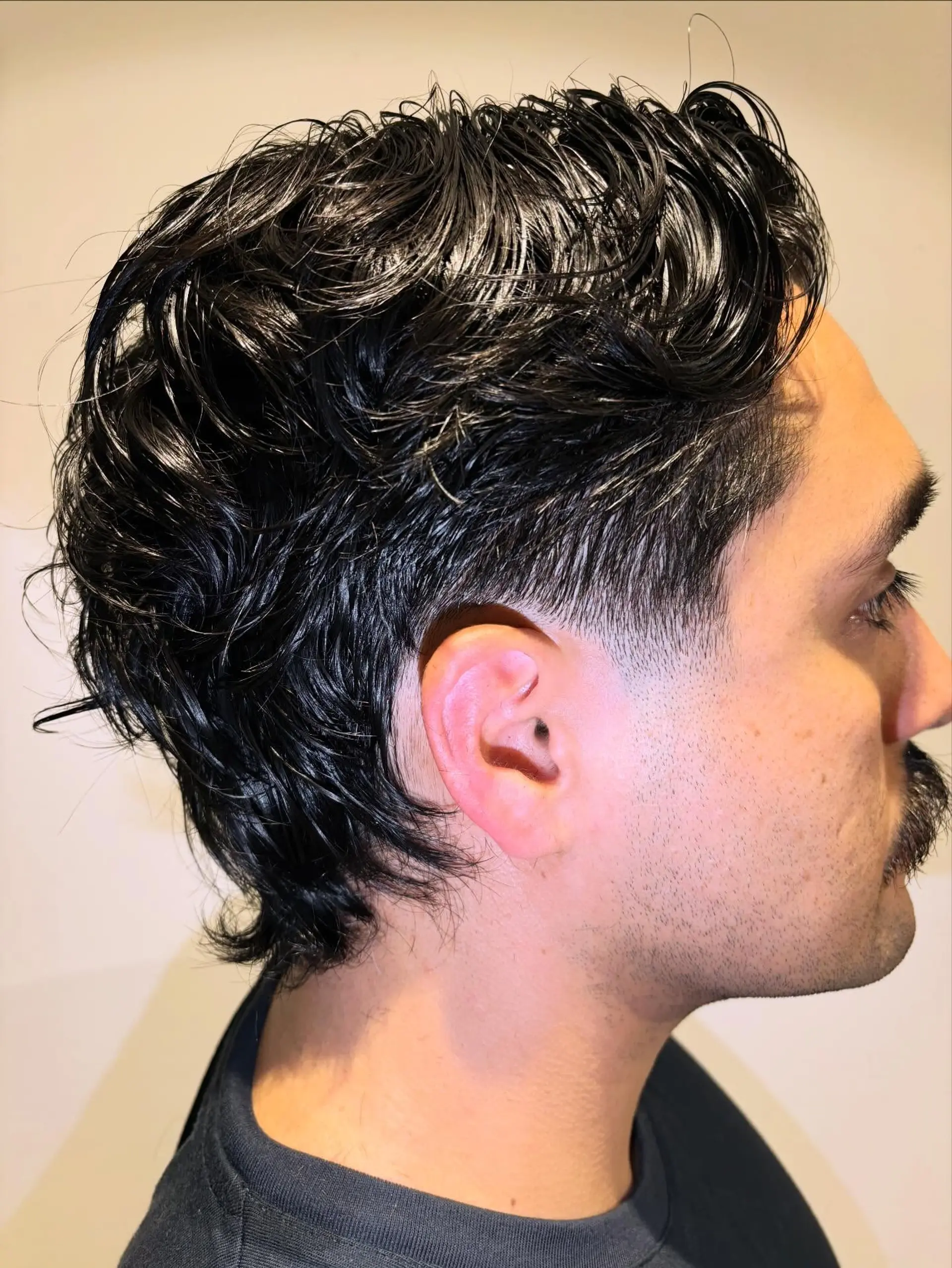 A textured, modern mullet haircut with a low taper fade and styled wavy locks. 1