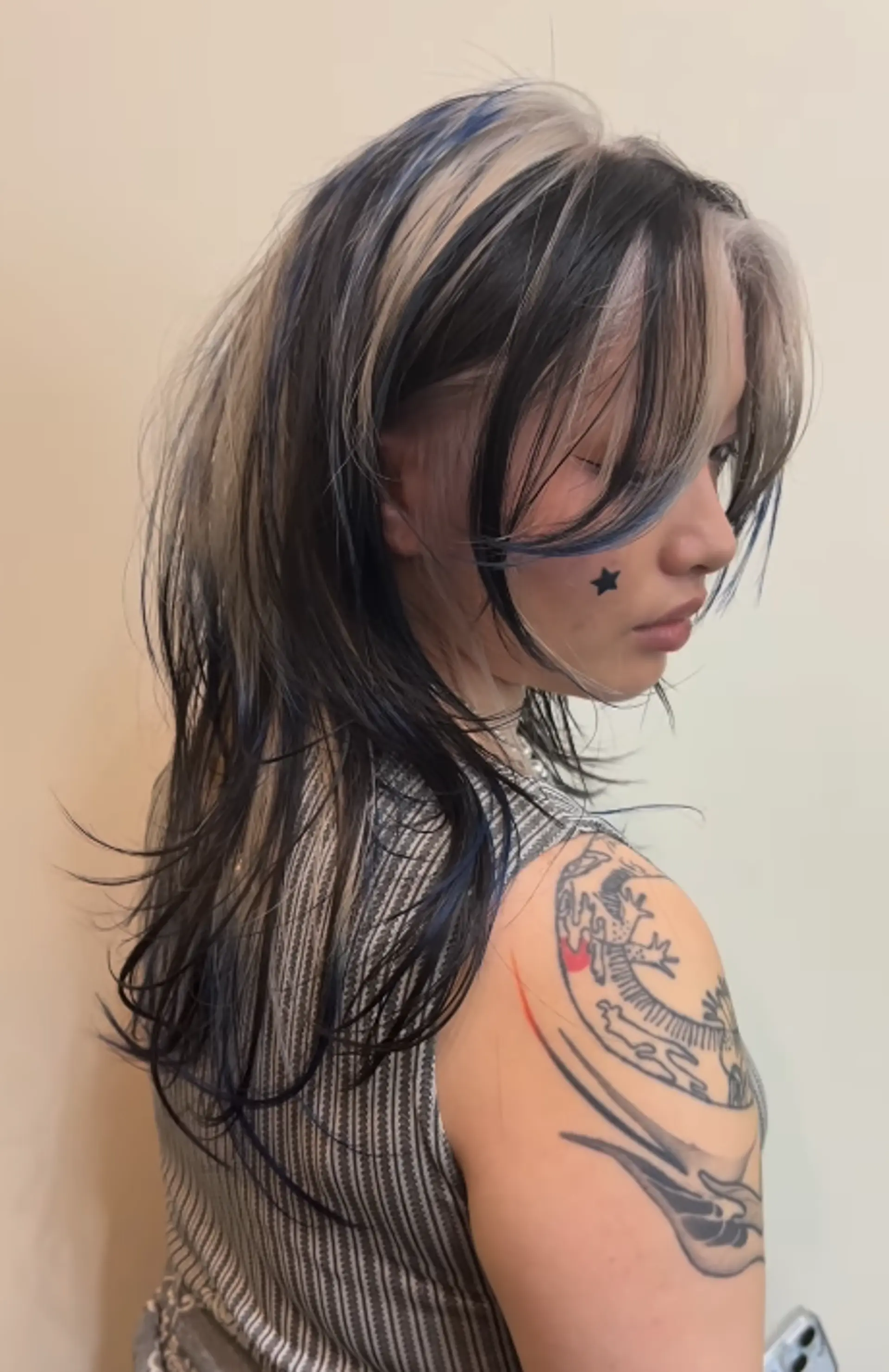 Long, wavy hair with layered, face-framing sections. Platinum blonde and black colors accented with blue highlights, giving a dynamic and bold appearance. 1