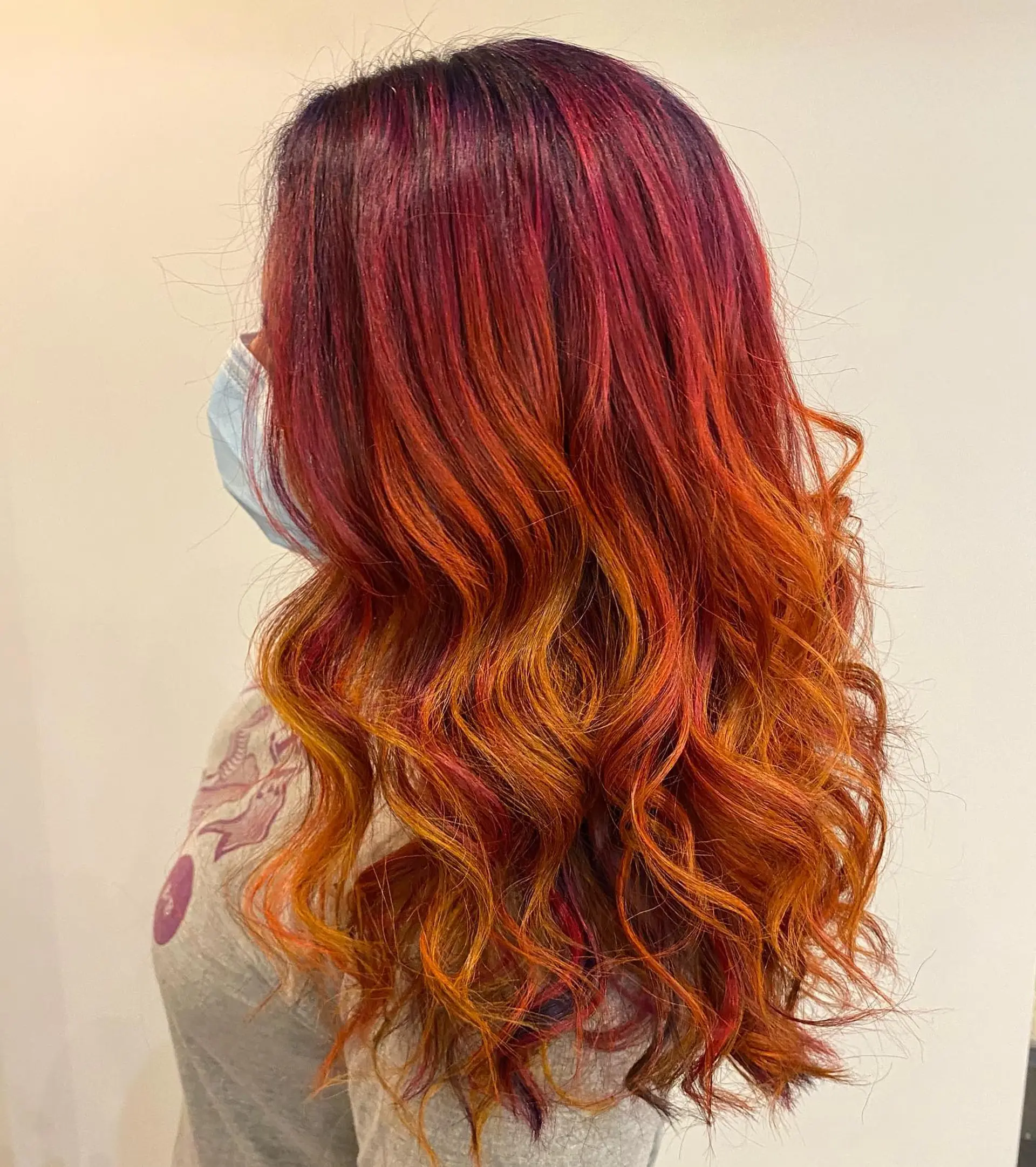 Long hair styled in soft, bouncy waves featuring a vivid autumn color melt from deep berry burgundy roots into blazing copper, orange, and golden ends. 1